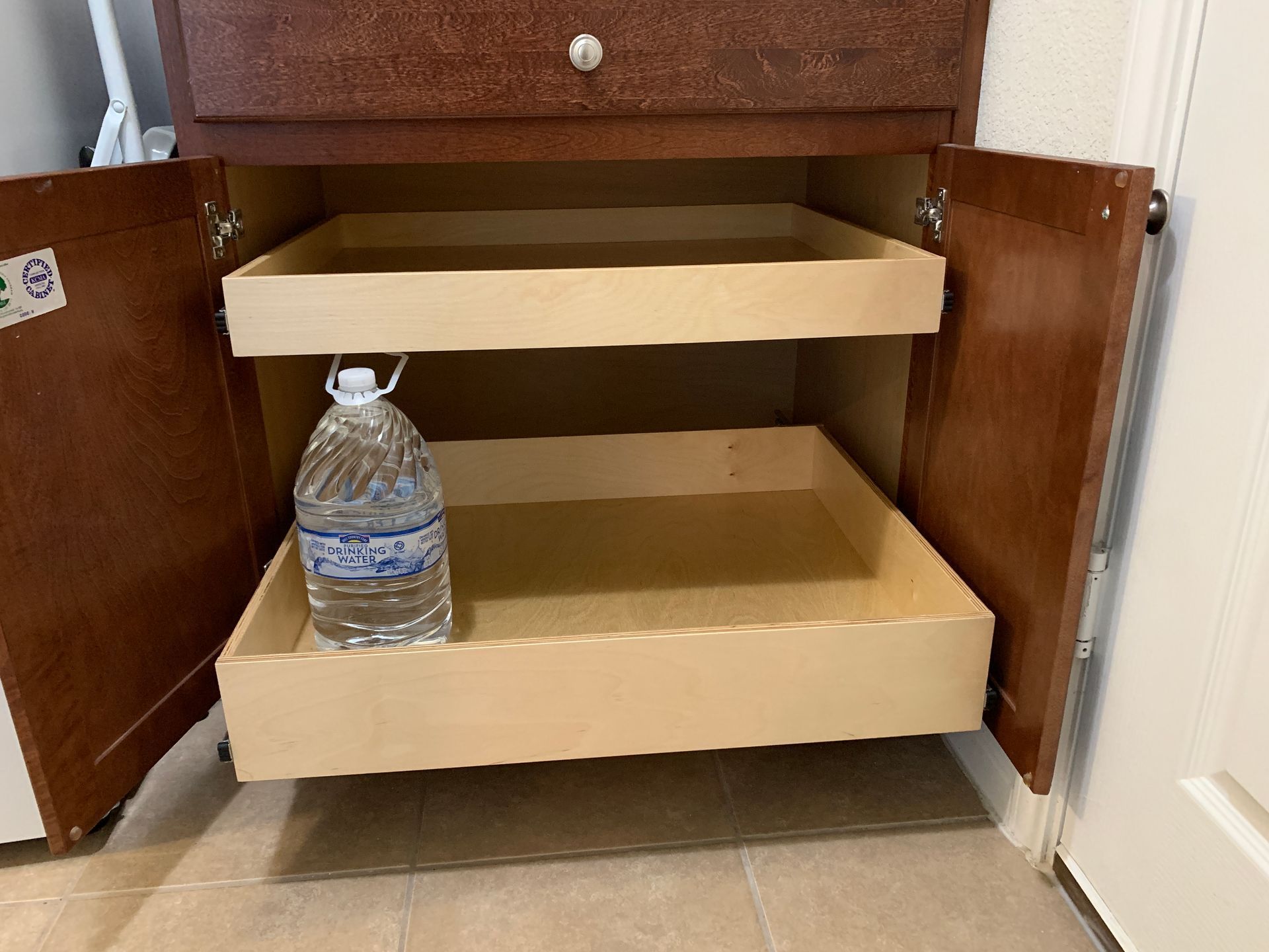Wooden kitchen cabinet with two pull-out shelves. A water jug sits on the bottom shelf.