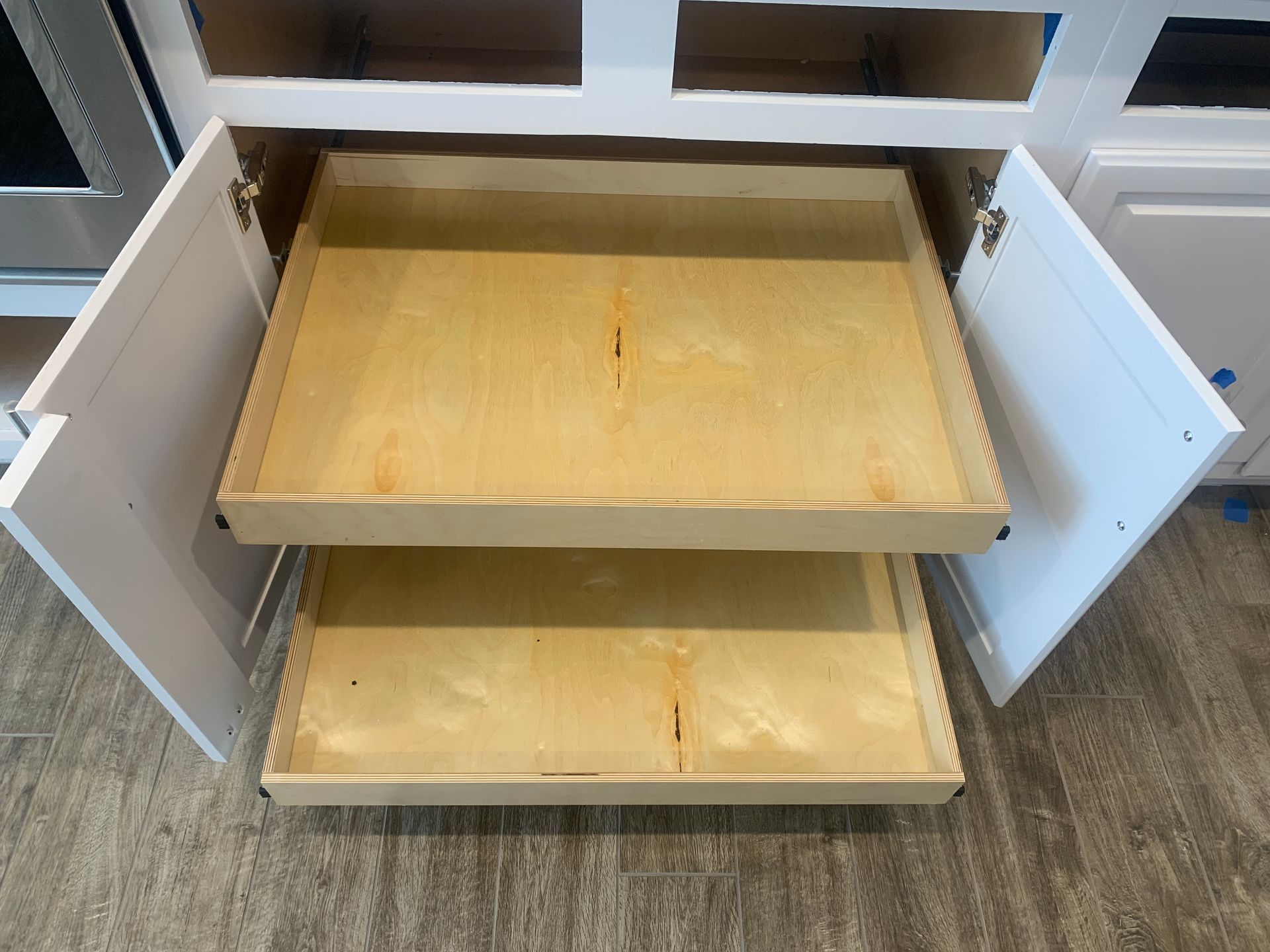 Open white kitchen cabinet with two pull-out wooden shelves.