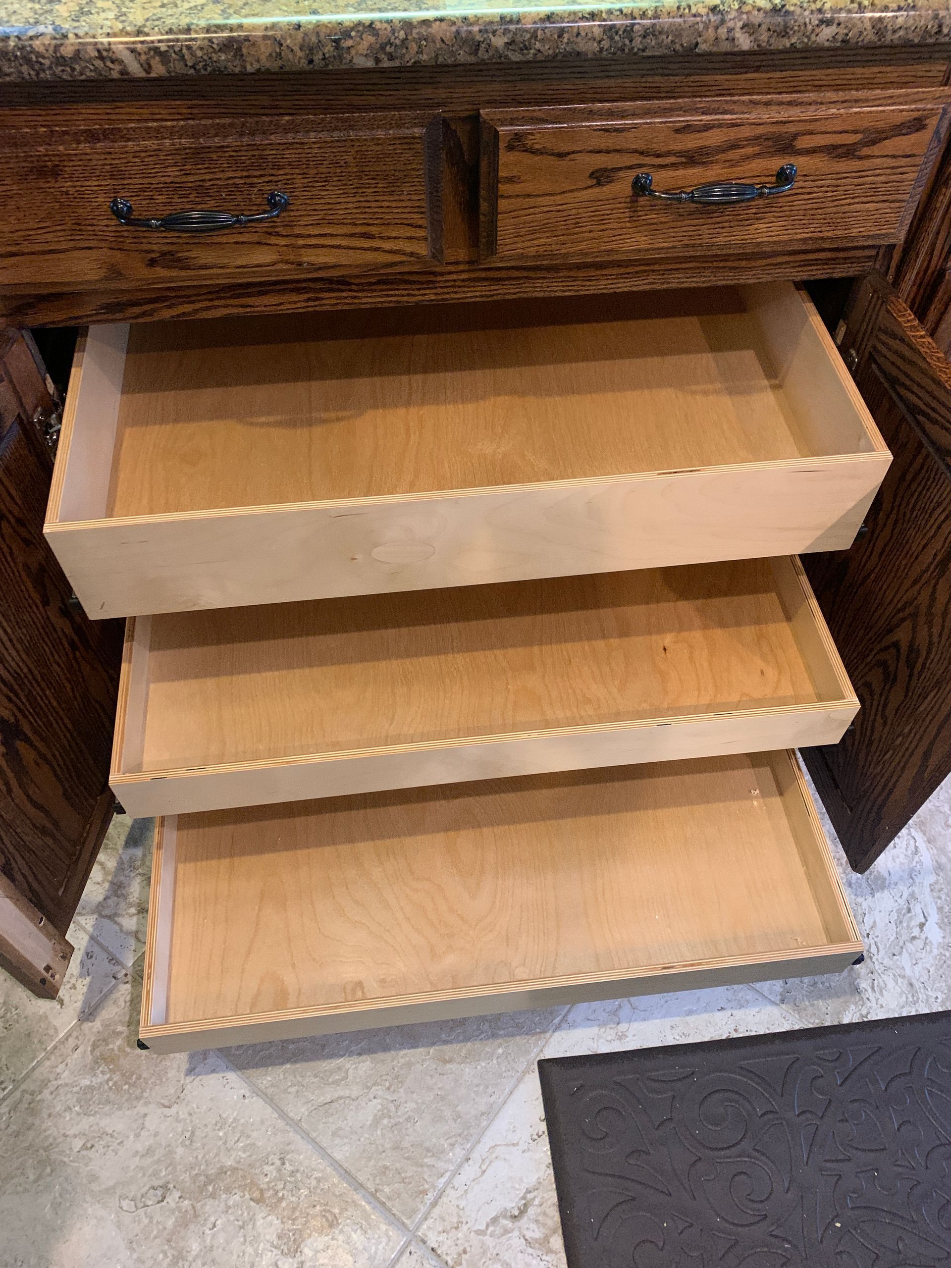 Wooden kitchen cabinet with three open, empty pull-out drawers.