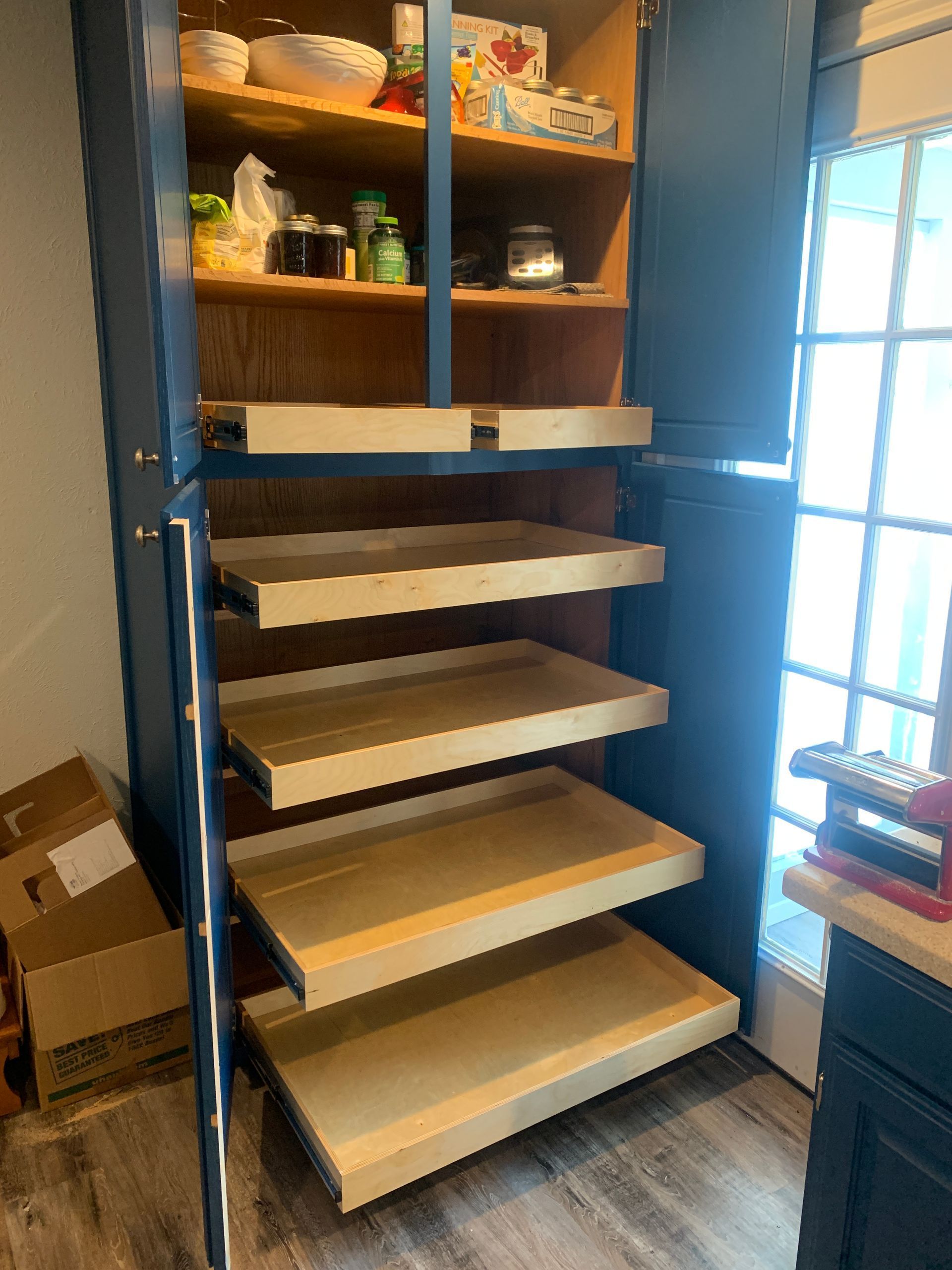 Blue pantry with pull-out shelves. Partially open, showing contents and the light wood shelves against the interior.
