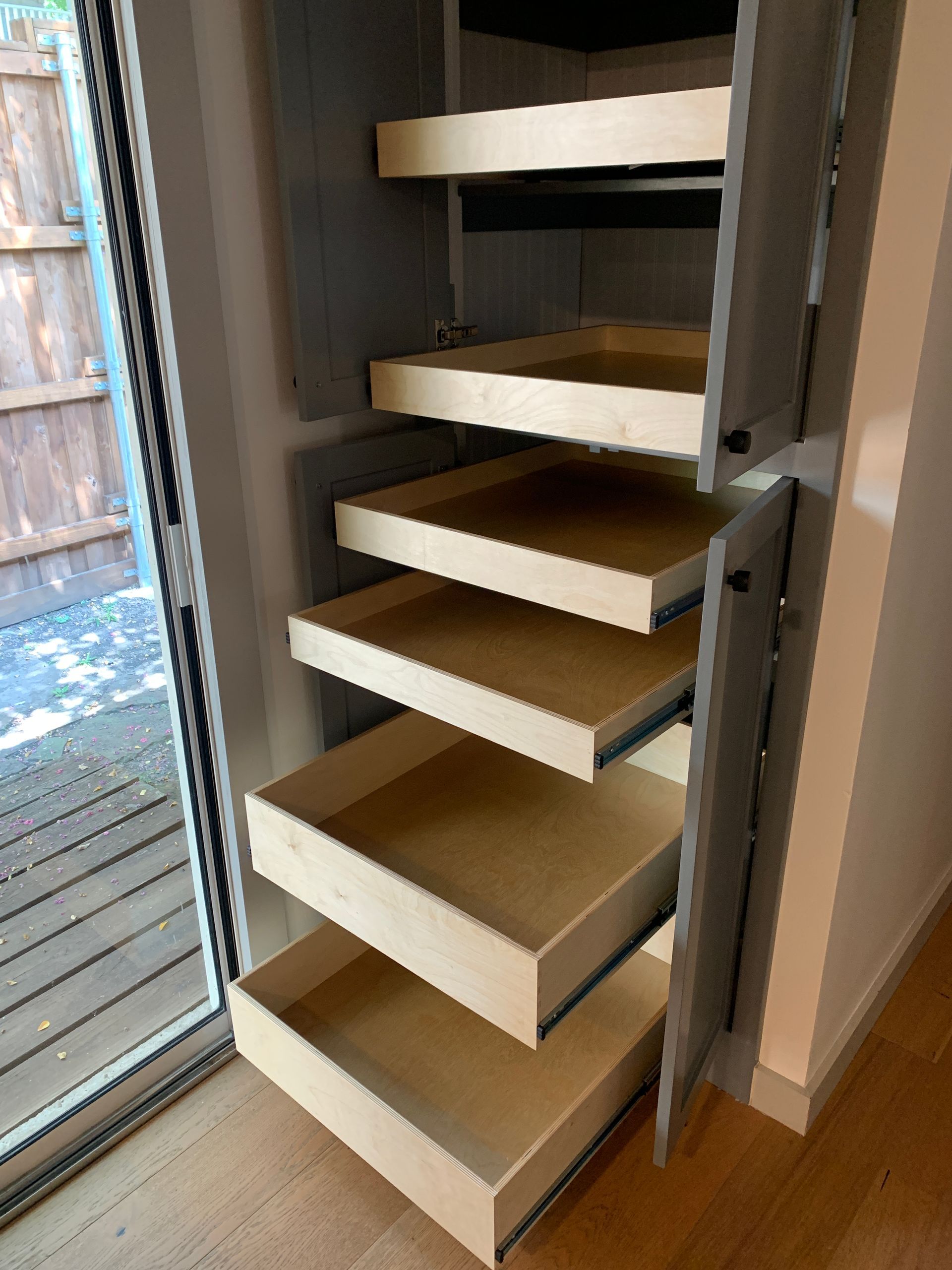 Gray pantry cabinet with pull-out shelves open; next to a sliding glass door.