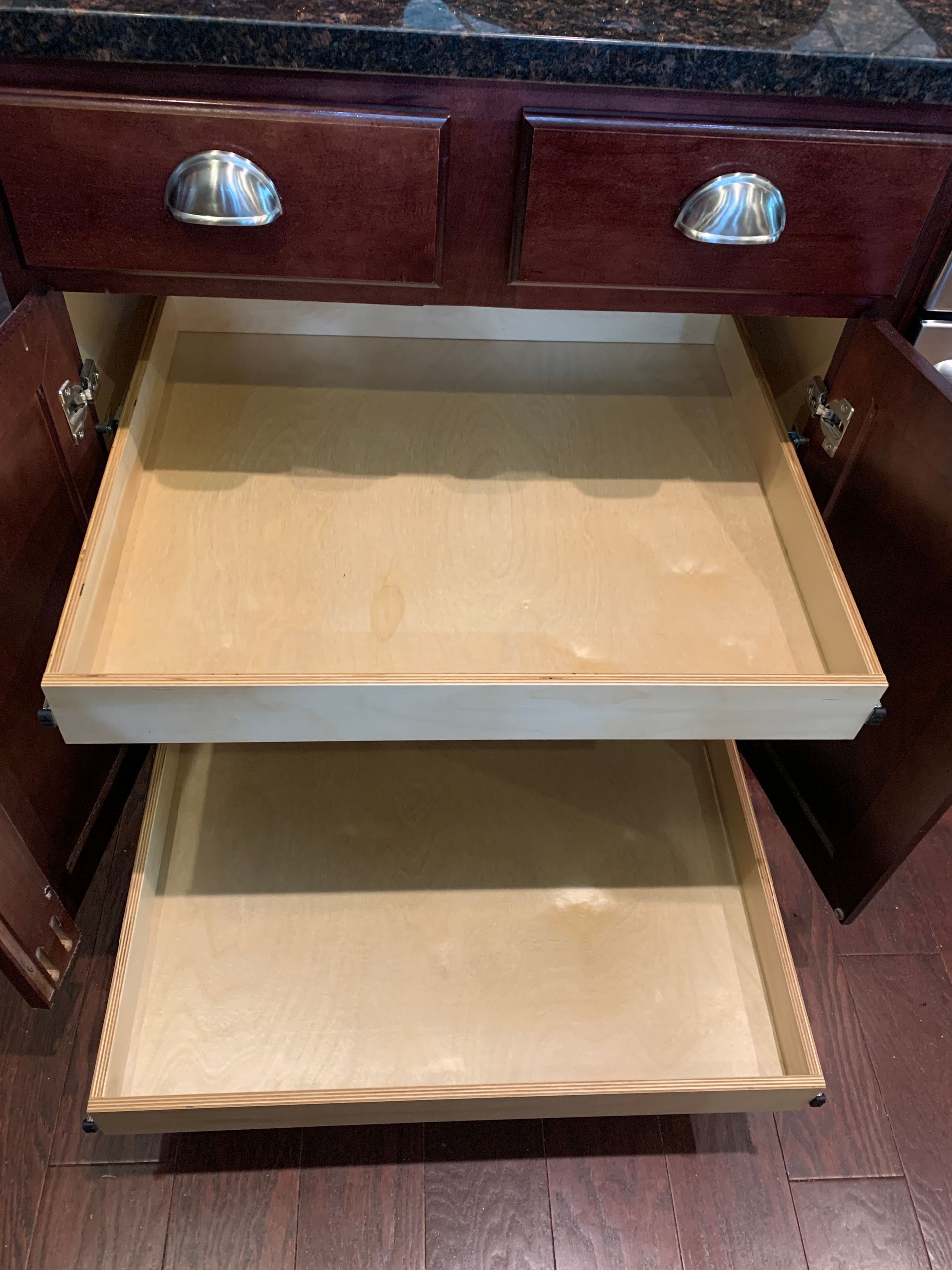 Open kitchen cabinet with two pull-out drawers, made of light wood, in a dark wood cabinet.