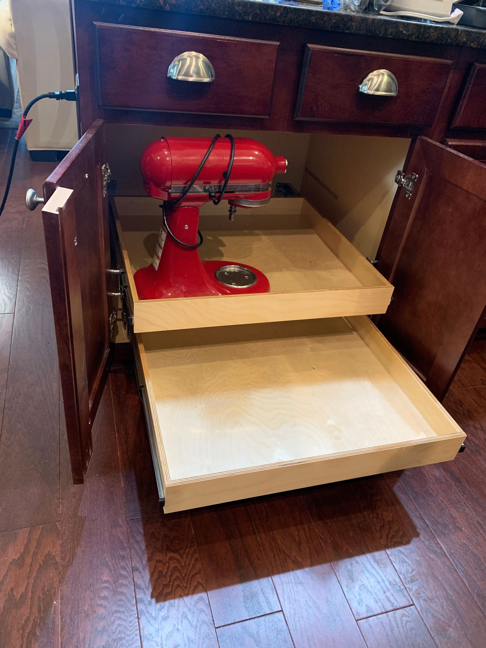 Red KitchenAid mixer on a pull-out shelf inside a dark wood cabinet.