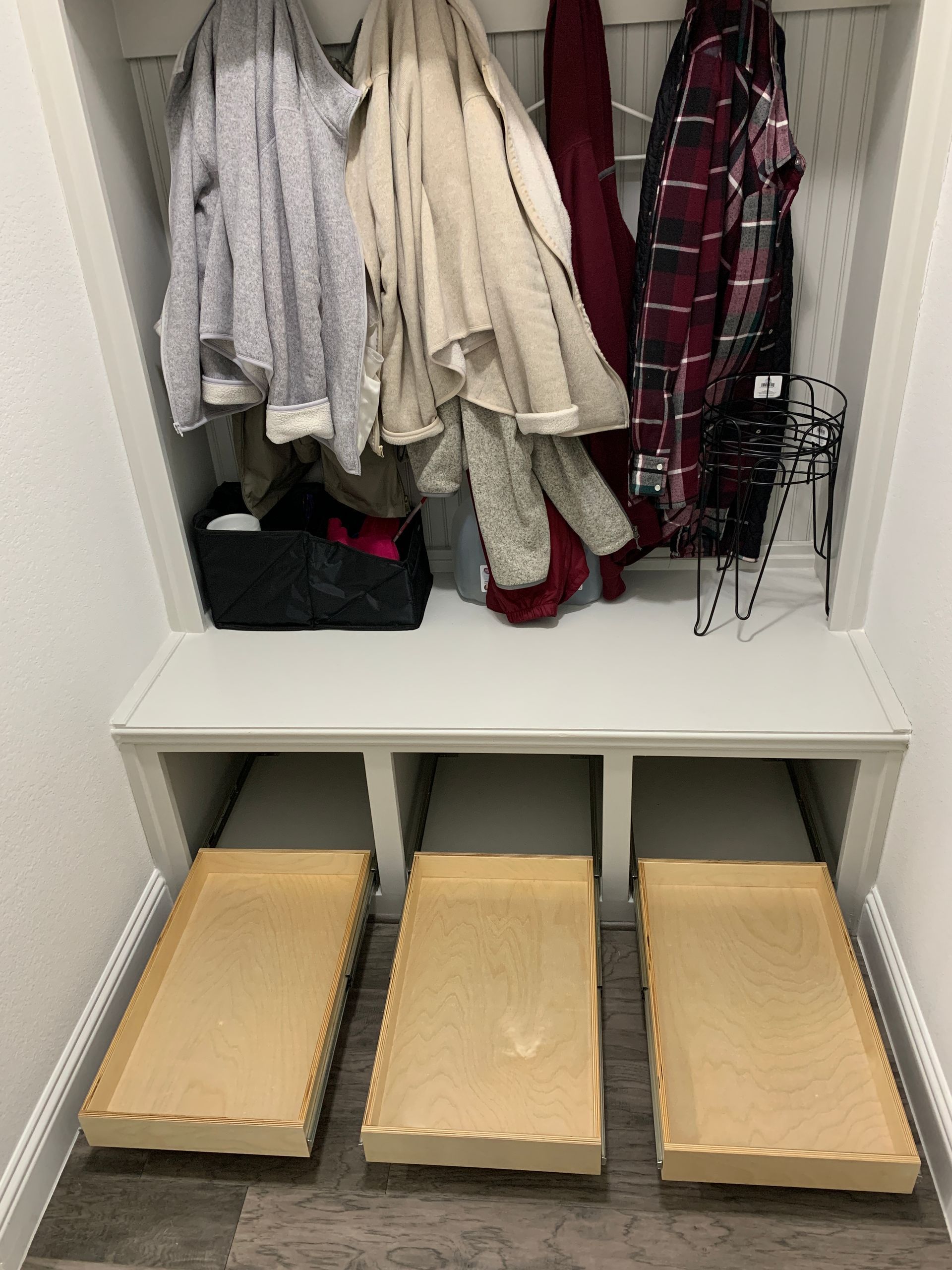 Built-in entryway storage unit with coat rack, bench, and three pull-out drawers. Coats hang above.