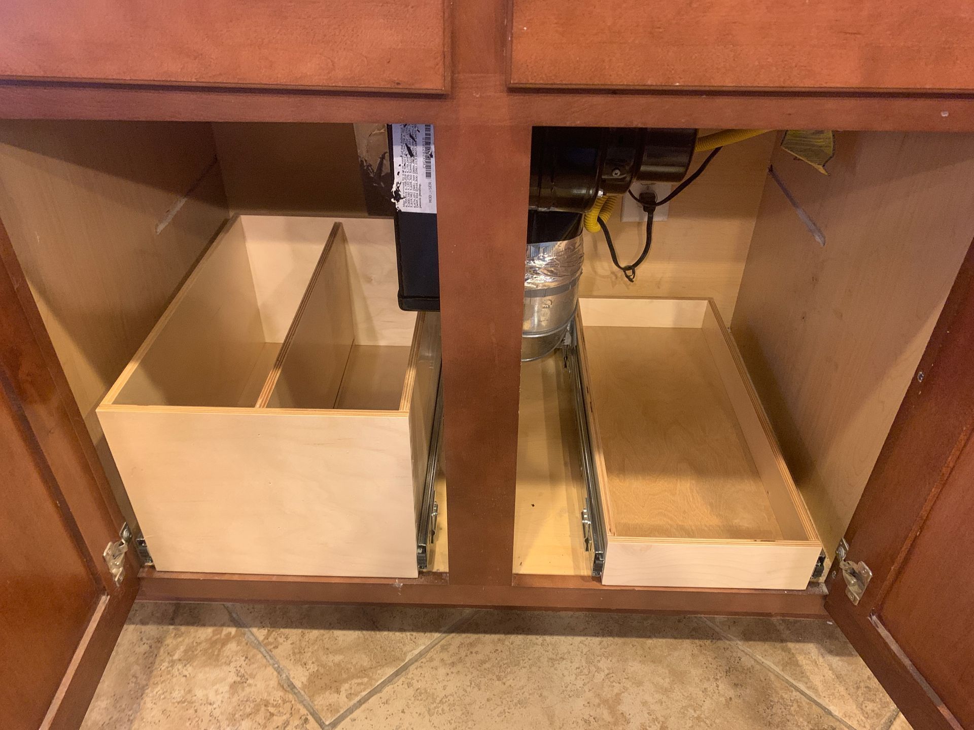 Kitchen cabinet interior with pull-out drawers and a large garbage disposal. Wooden construction.