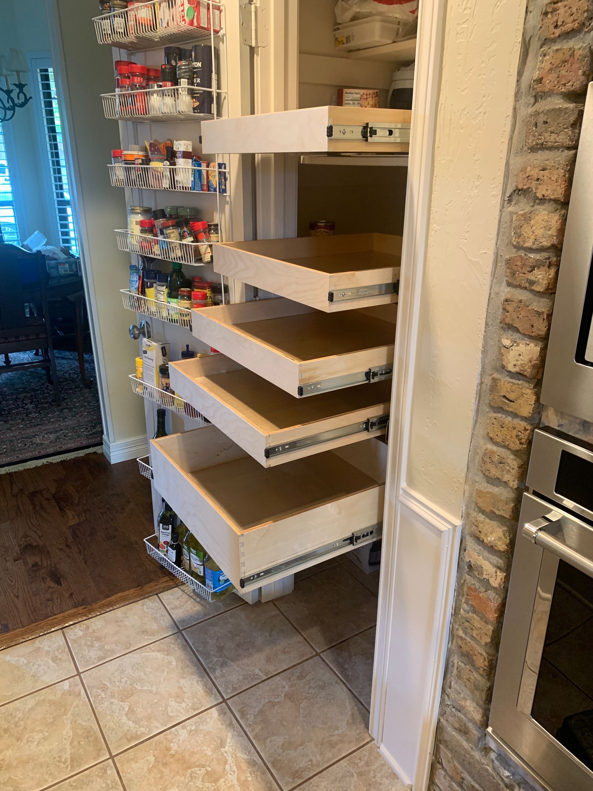 Kitchen pantry with pull-out drawers and rotating spice rack; hardwood floor, brick wall.