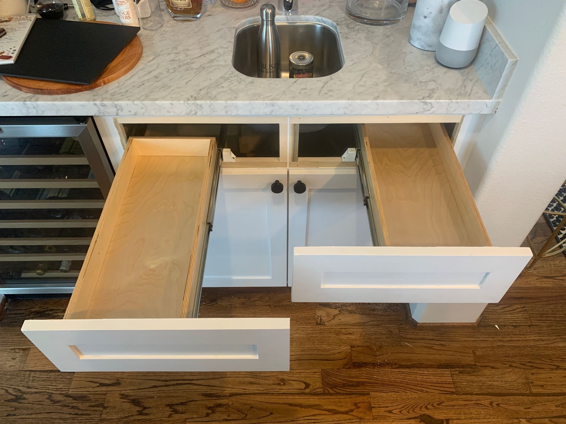 White cabinet with two open drawers under a sink, wooden floor.