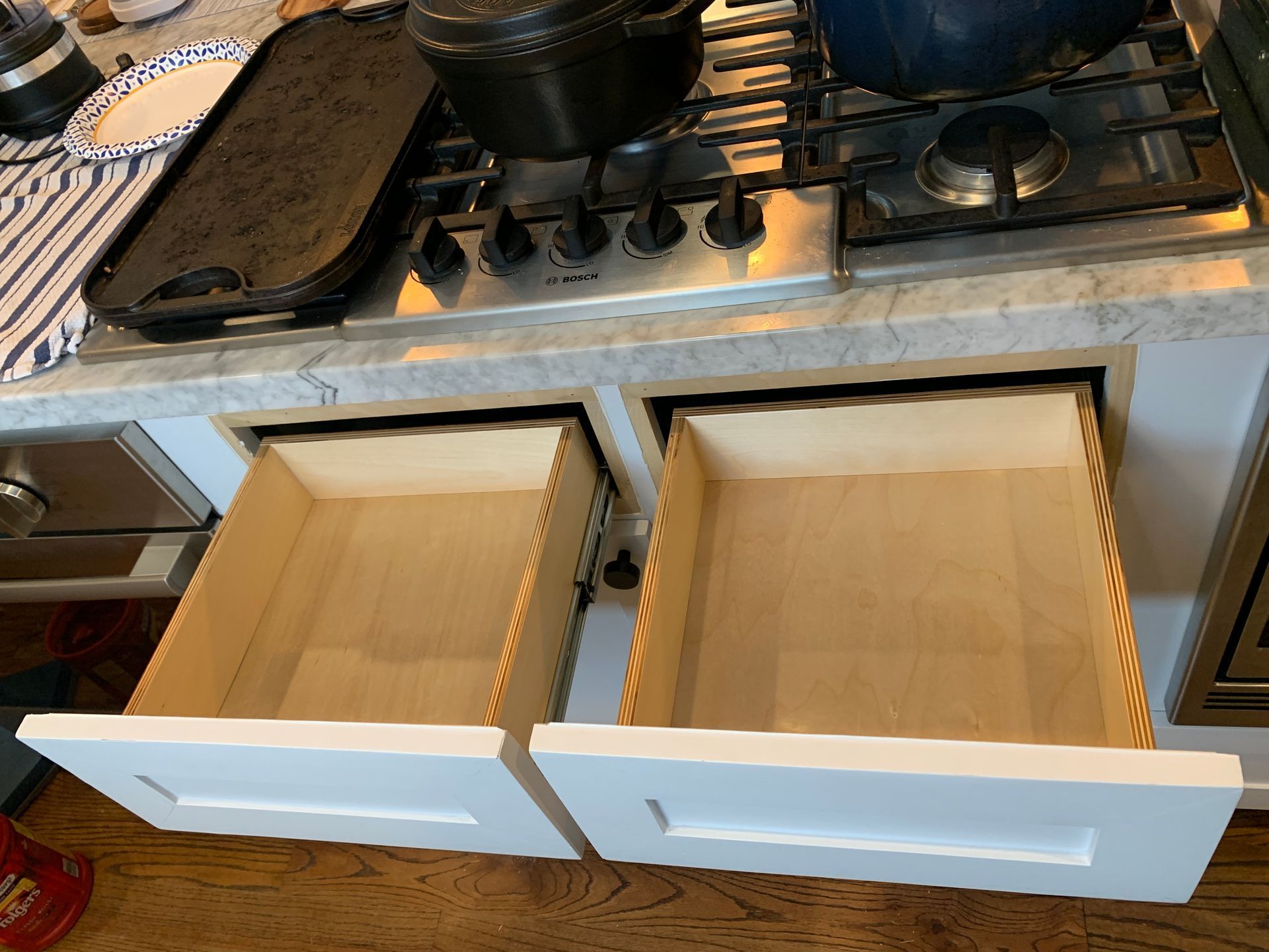 Two open white kitchen drawers below a stovetop, wood interior.