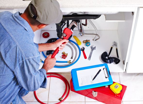 Plumber working under a sink, using a wrench. Various tools and supplies are in the cabinet.