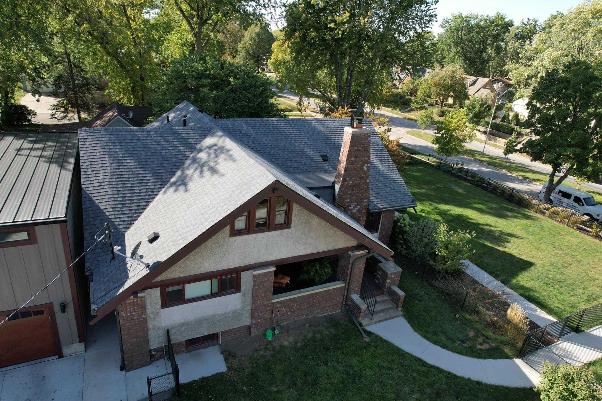 Aerial view of a house with gray roof, brick walls, and a curved walkway surrounded by trees and lawn