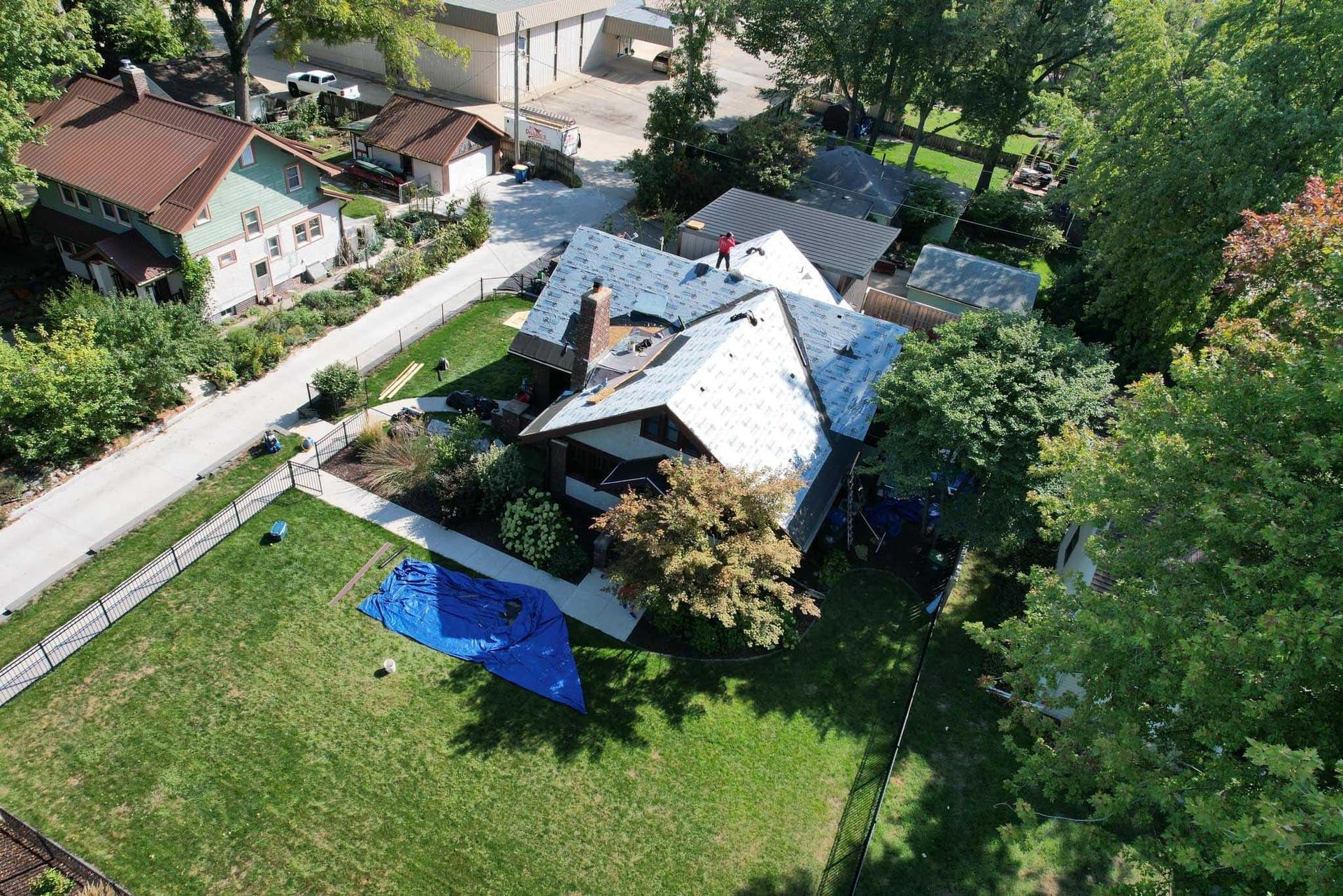 Aerial view of a house with a gray roof, green lawn, and surrounding trees in a suburban neighborhood