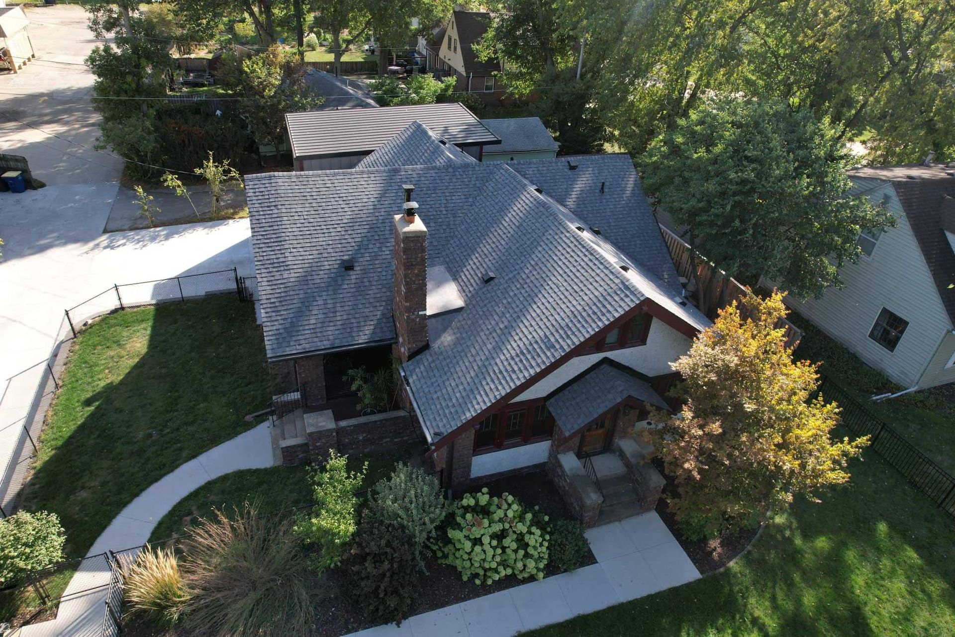 Aerial view of a house with a gray roof, brick chimney, and landscaped yard with curved walkways