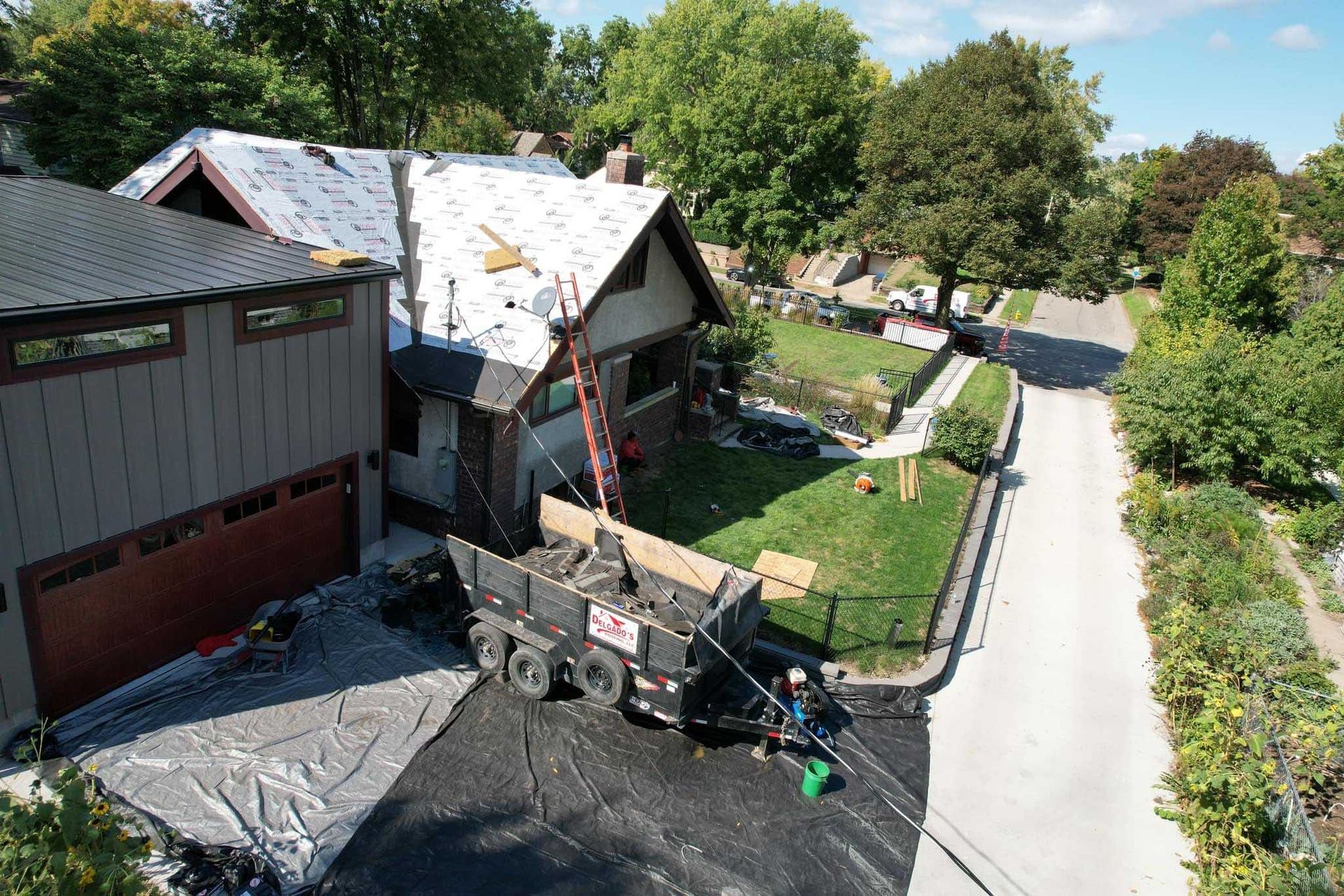 Aerial view of a suburban house with a driveway, yard, and tree-lined street.