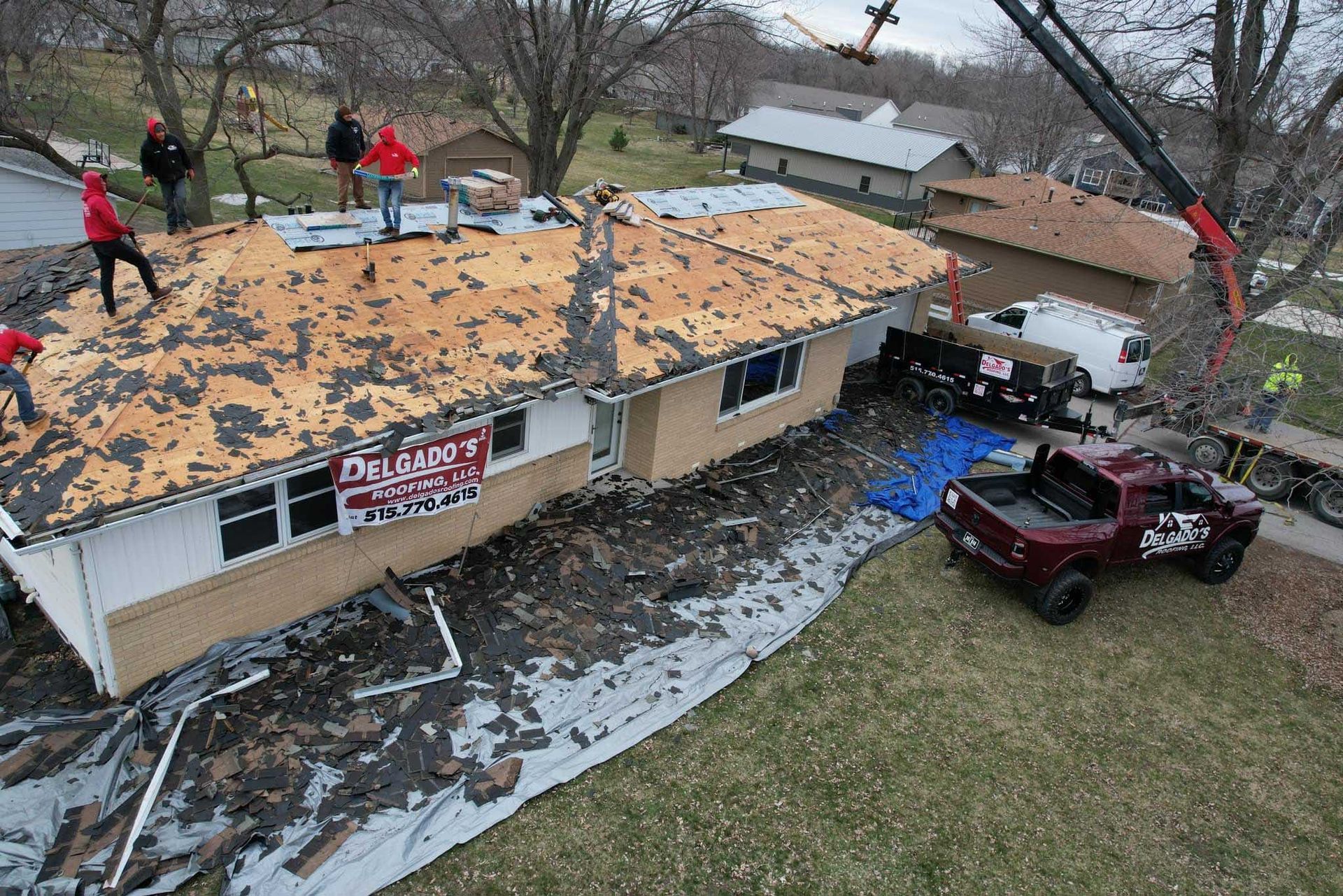 Workers replacing a roof with new shingles on a house, with ladders, debris tarps, and a truck below.