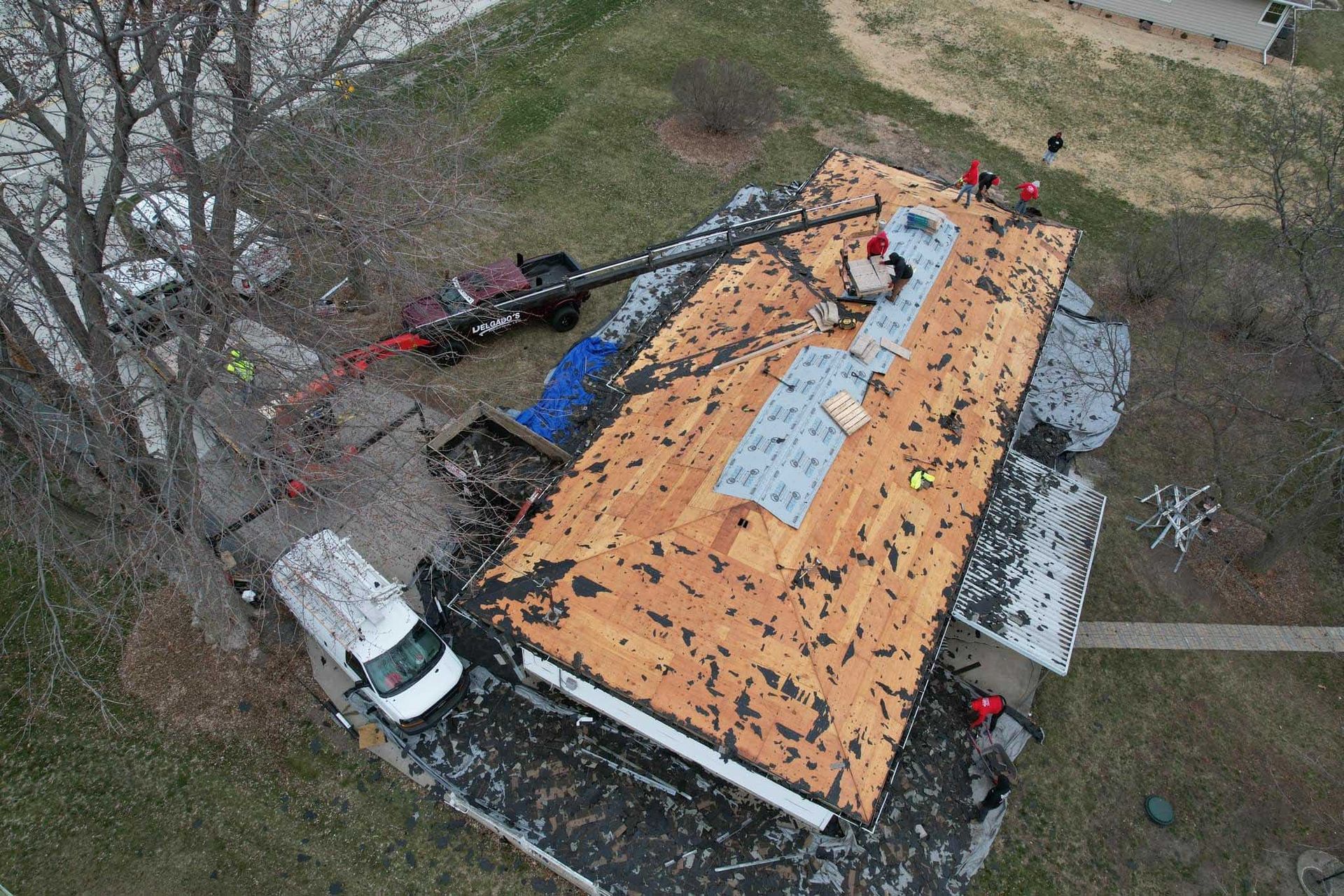 Aerial view of a damaged roof with orange tarp, debris, and a white van beside a tree.