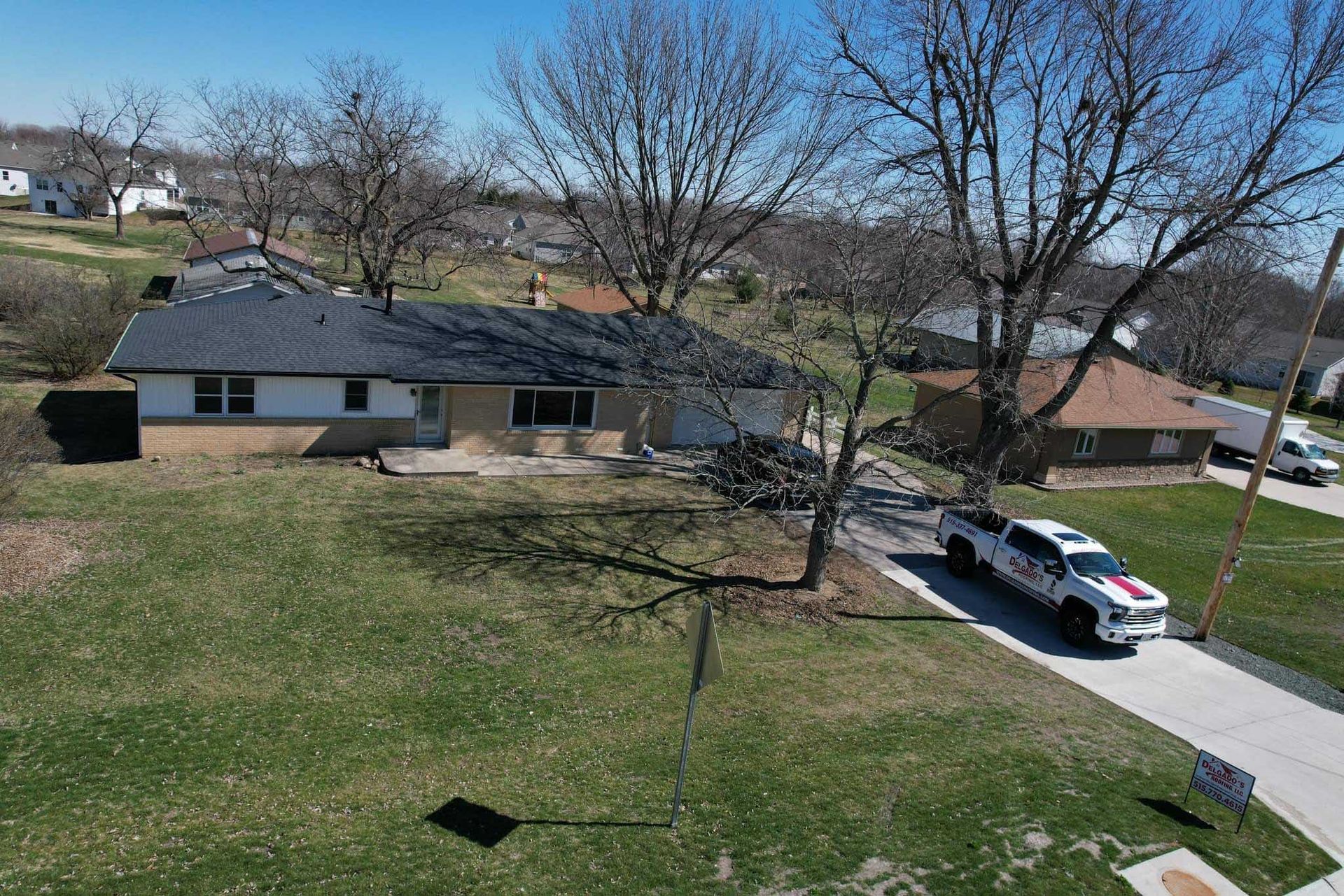Suburban house with bare trees, a driveway, and a white SUV parked outside on a sunny day