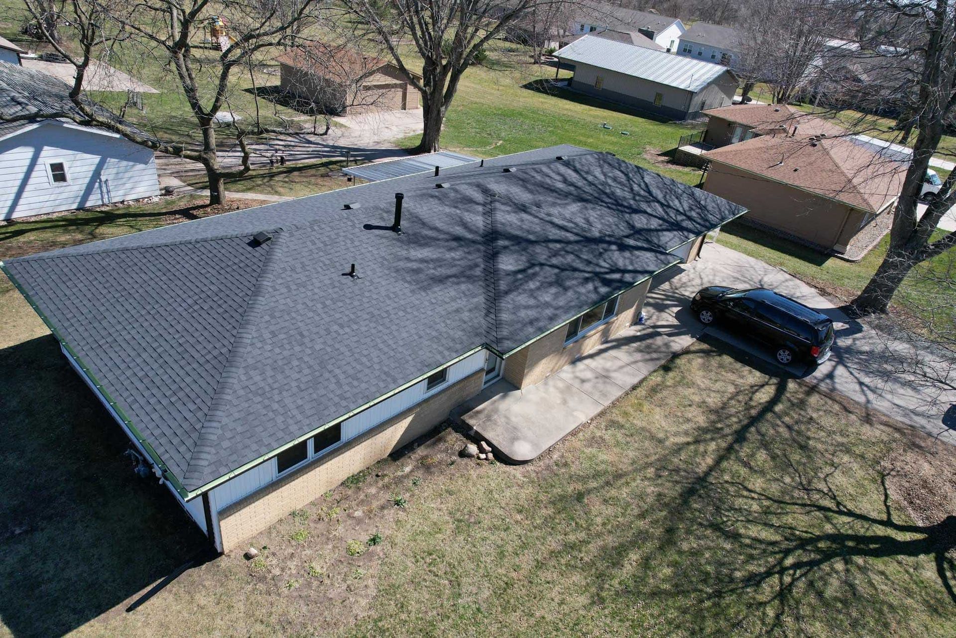 Aerial view of a gray-roofed house with a black SUV parked by the driveway and trees casting shadows.
