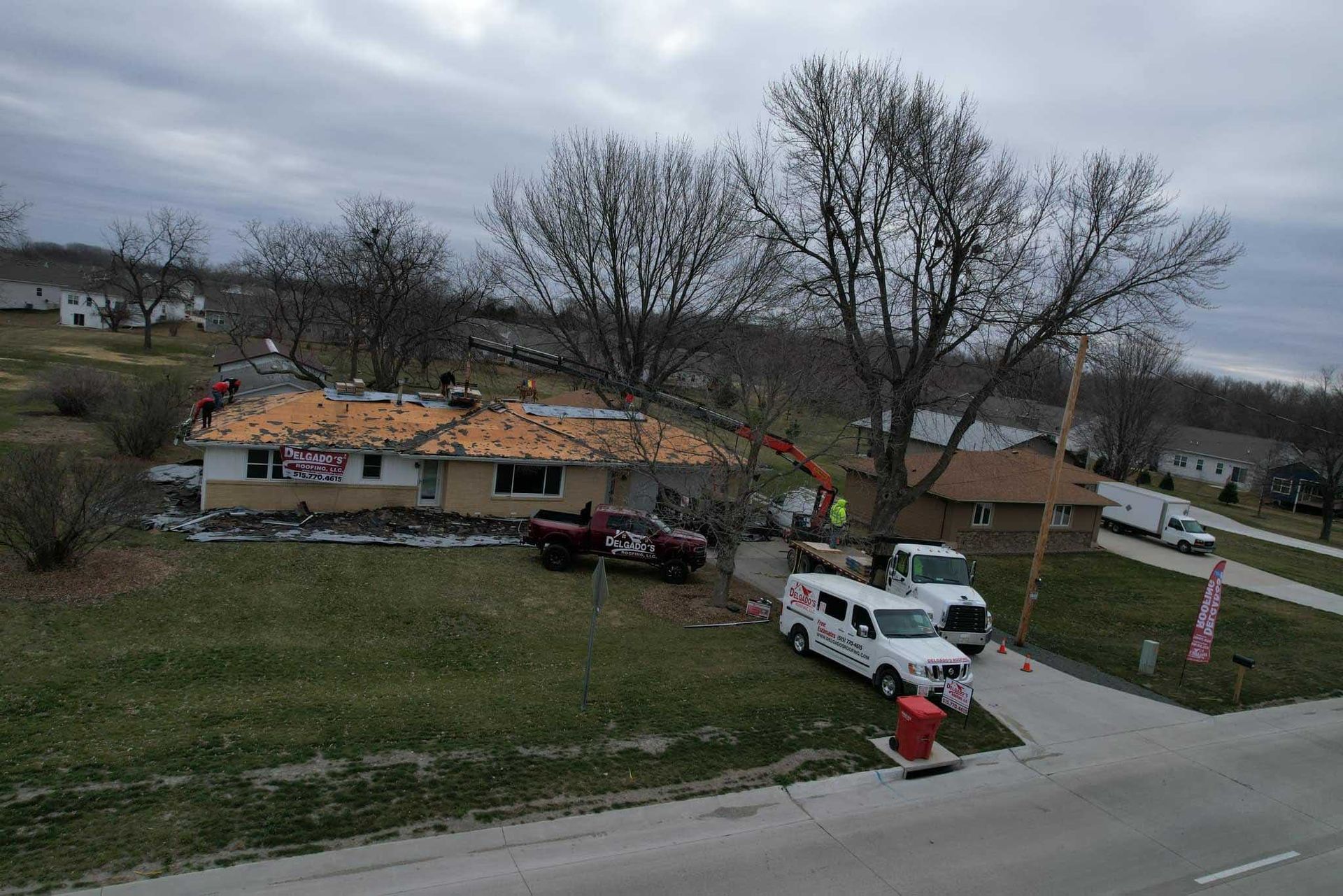 Damaged house with exposed roof, parked vehicles, and debris in a rural roadside yard