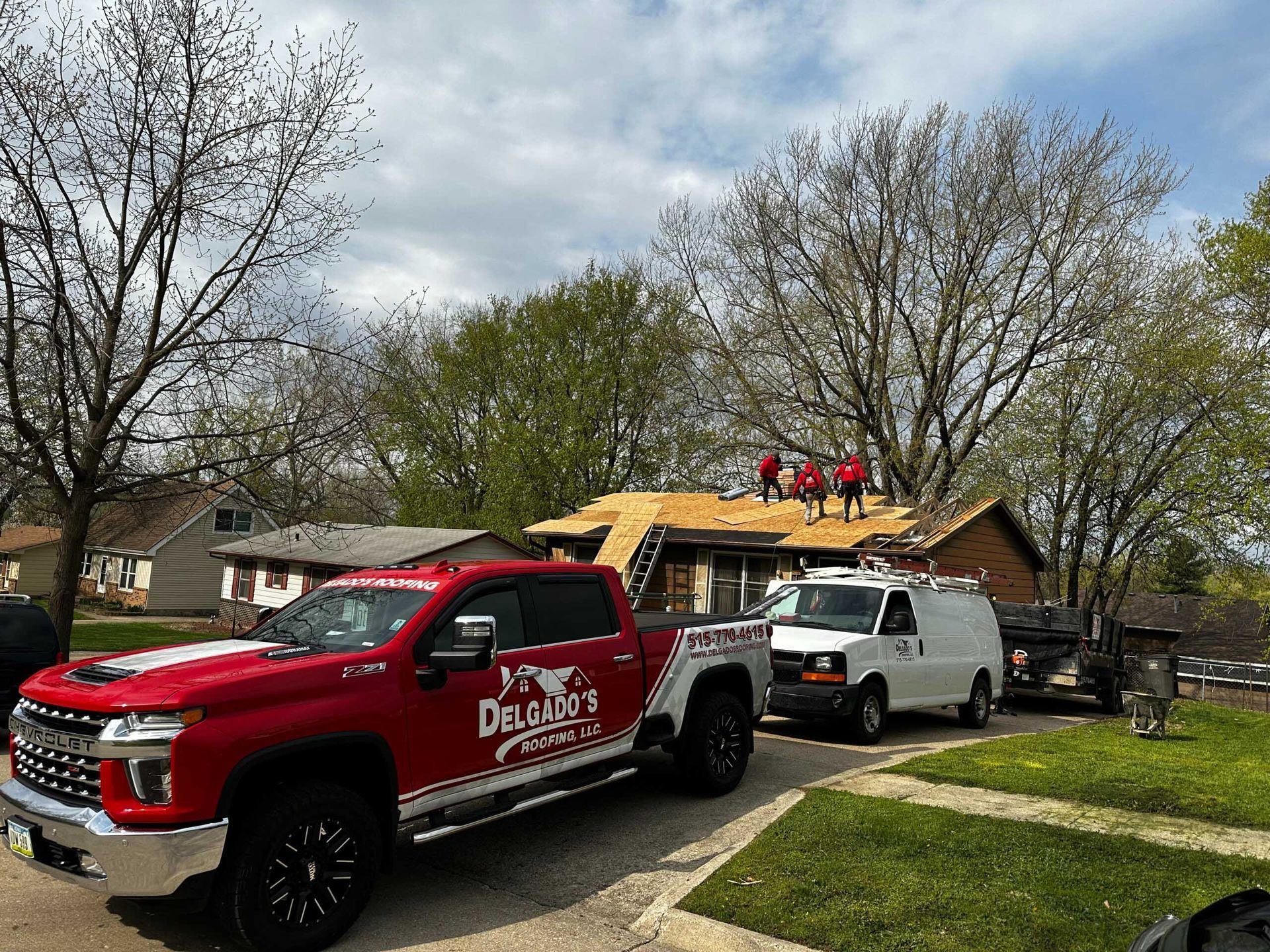 Red and white utility trucks parked by a house with workers on the roof amidst storm damage.