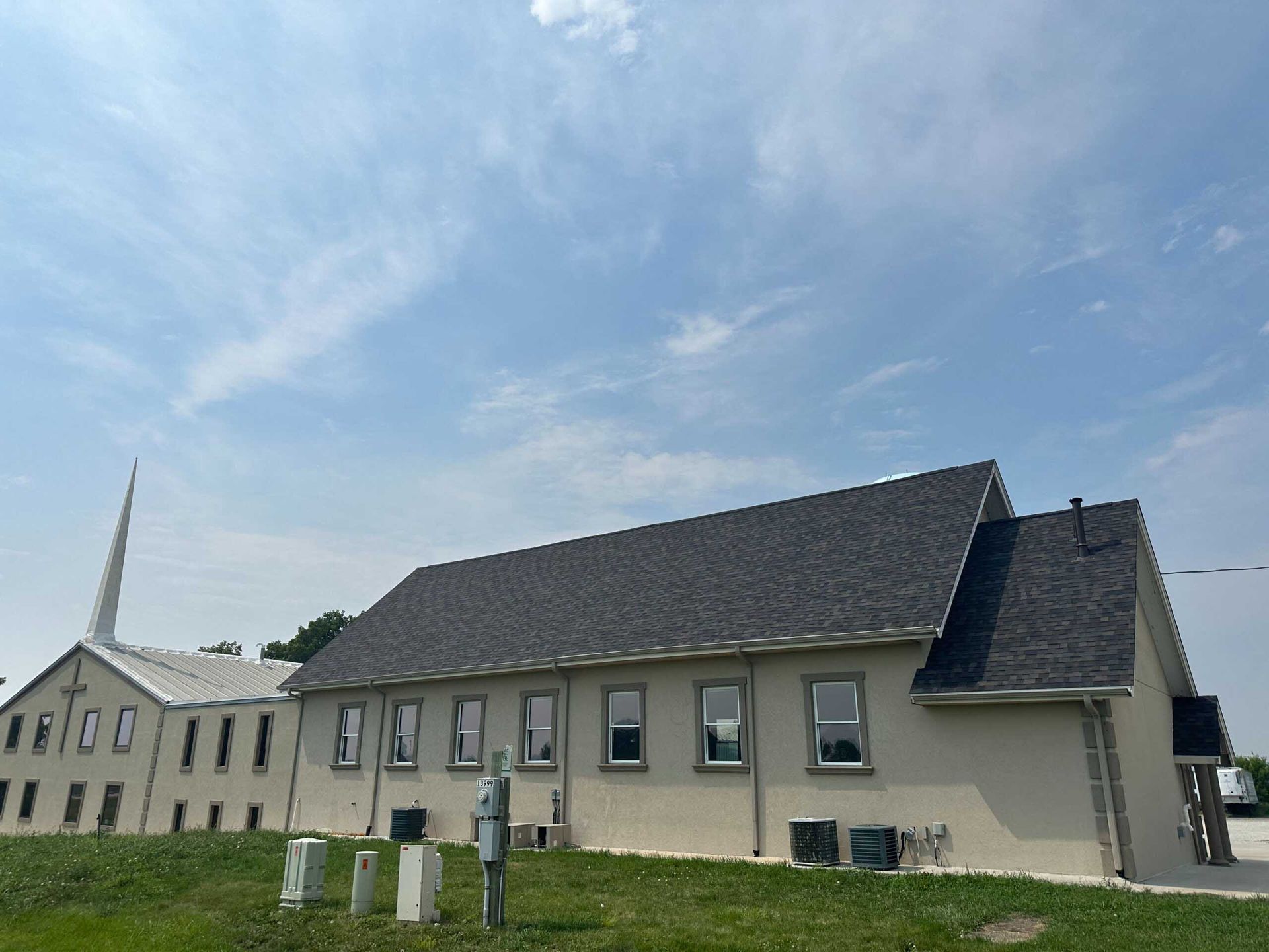 Low beige building with gray roof on a grassy field under a cloudy sky