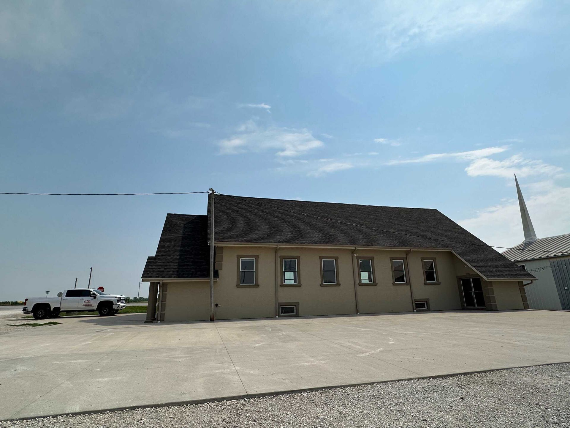 Low beige building with a dark roof beside a wide concrete lot under a blue sky
