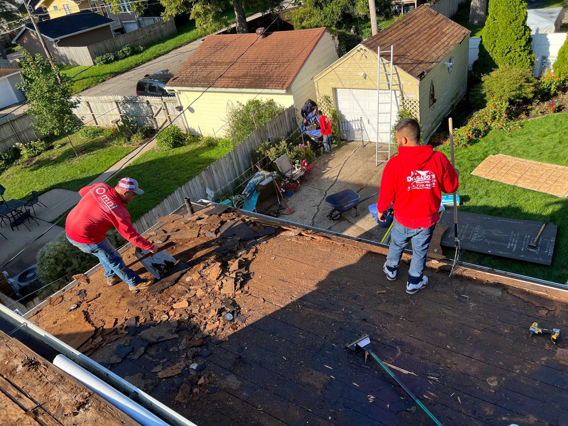Two workers in red shirts repair a flat roof with tools and debris nearby.