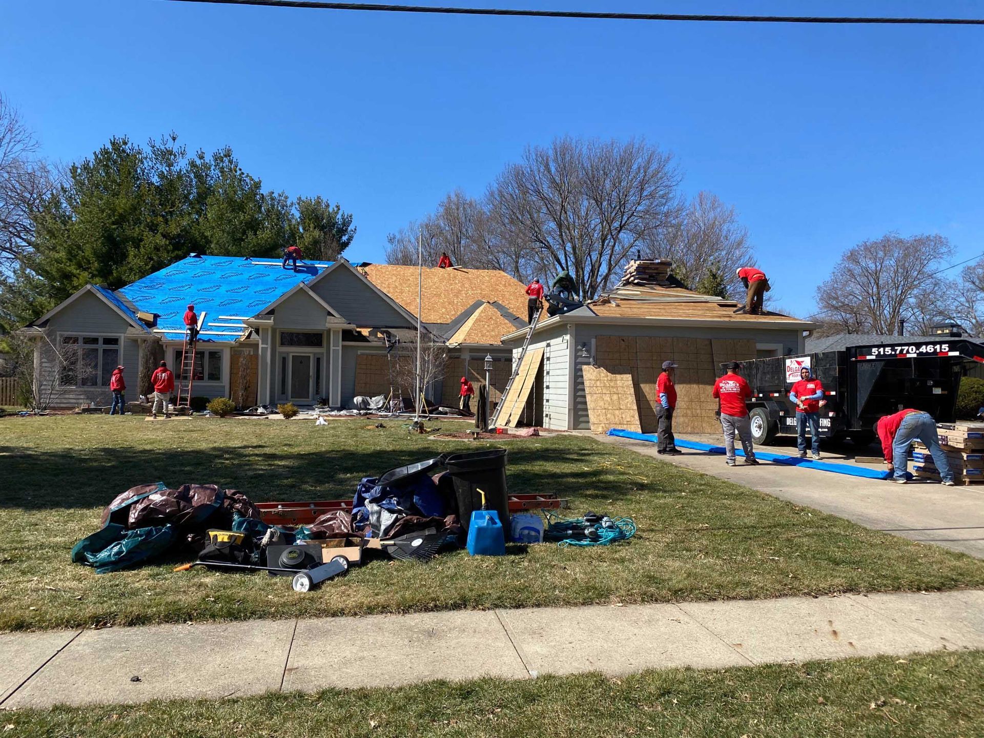 Roofing crews working on damaged houses, with tools and materials spread across the front lawn.