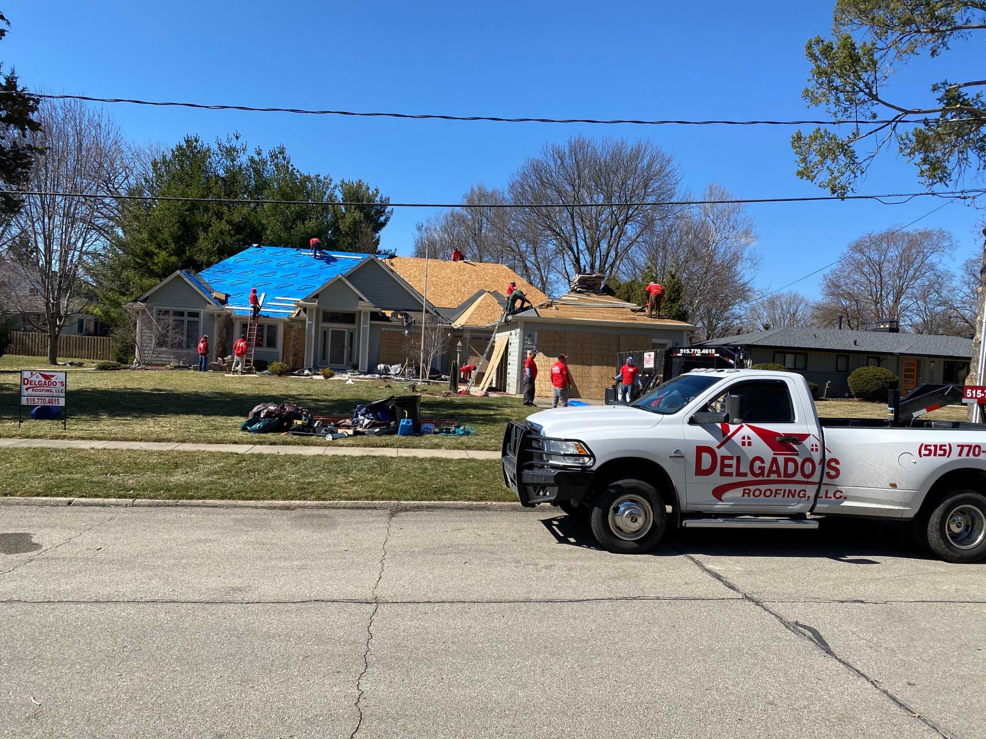 Delgados cleanup truck parked outside storm-damaged house with blue tarp on roof and debris in yard