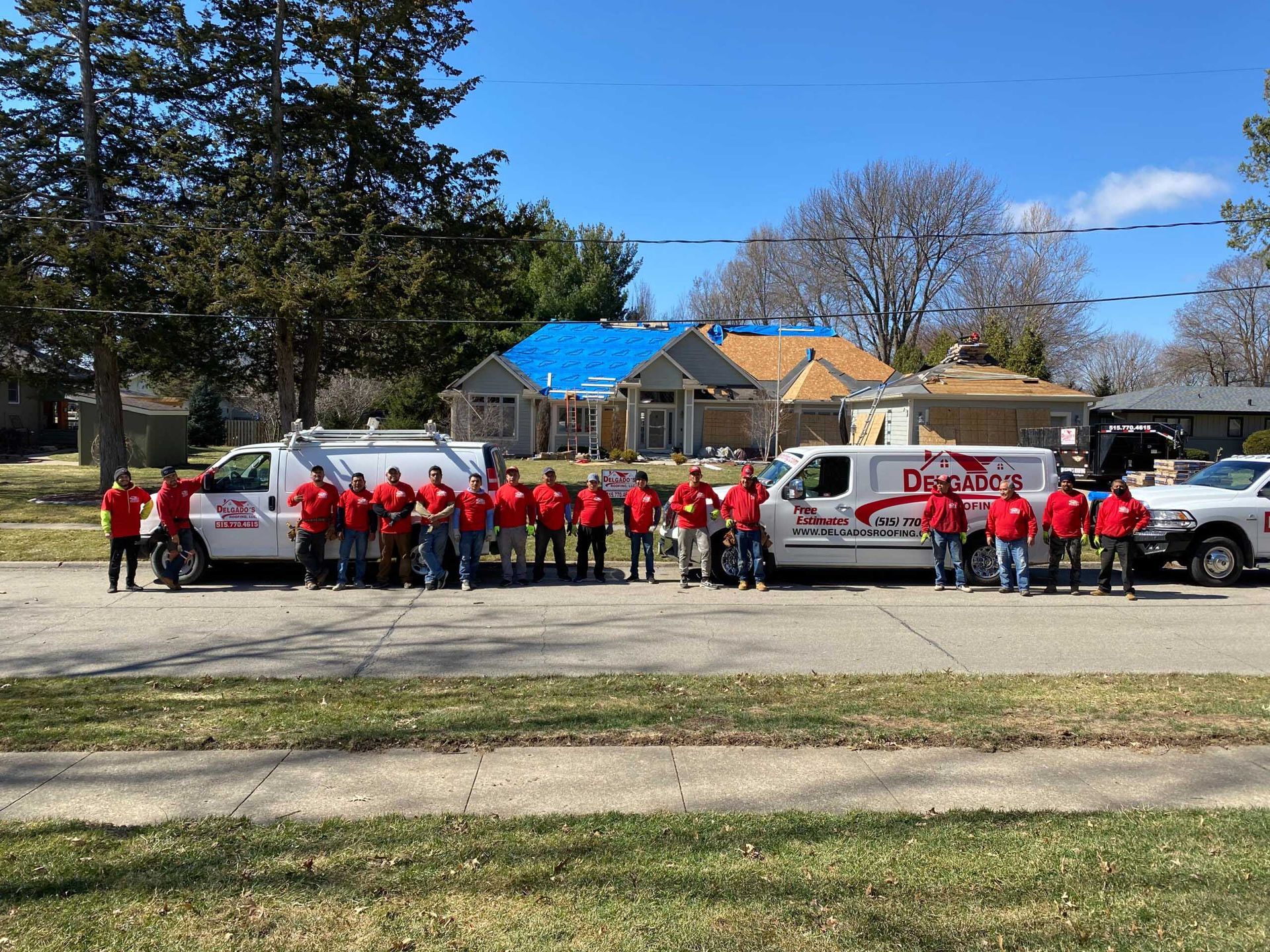 Group in red shirts posing with two white trucks on a roadside under a clear blue sky.