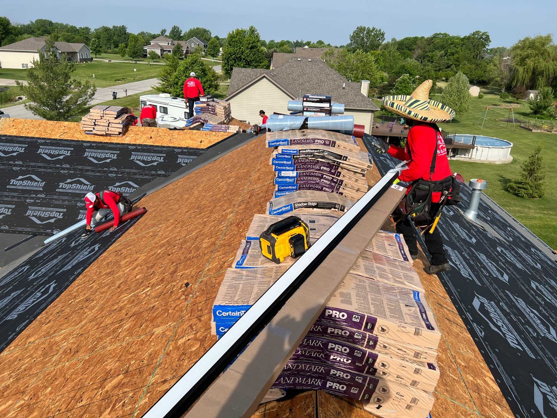 Workers installing roofing on a house, with black underlayment and shingles stacked along the ridge.