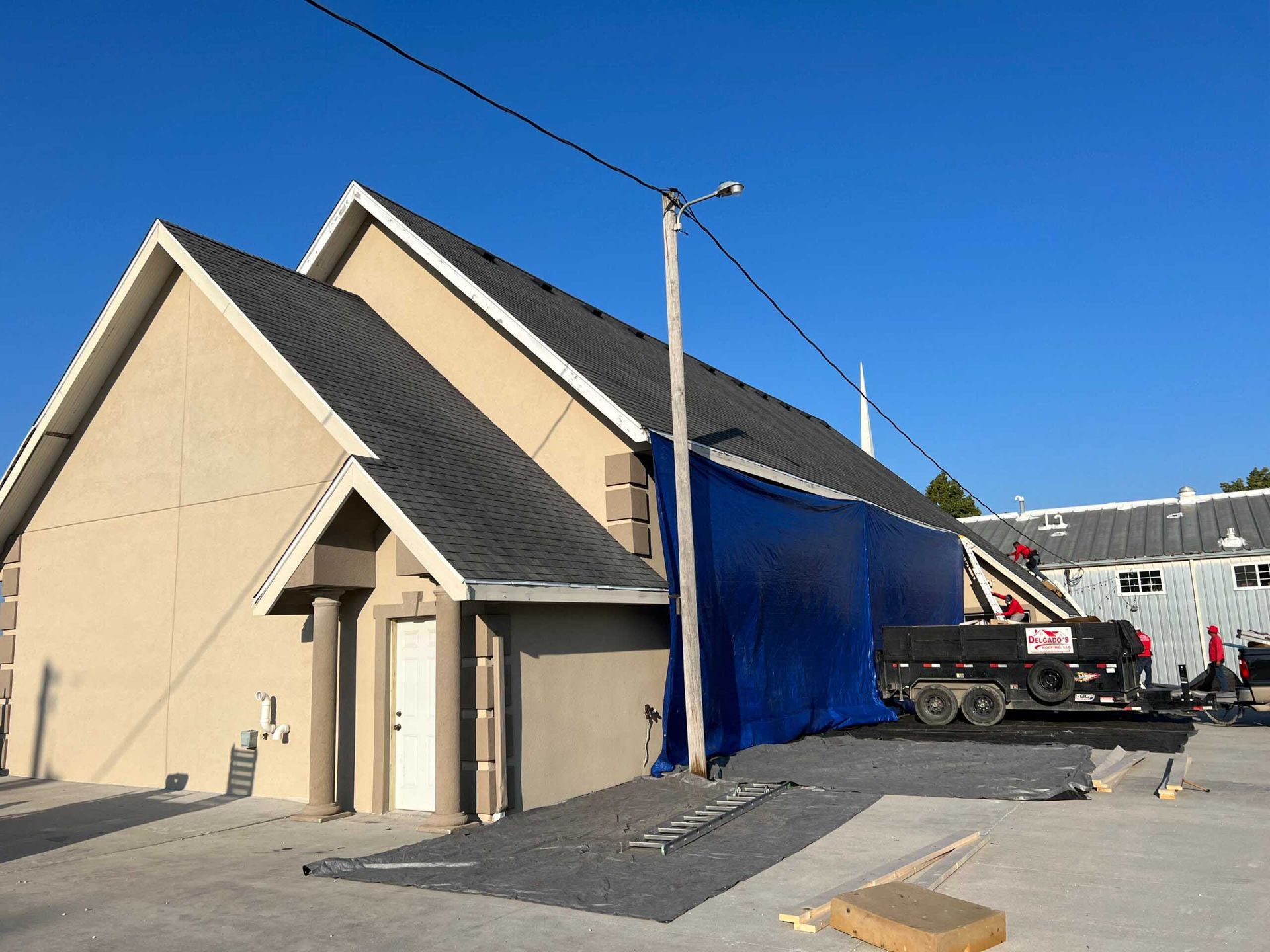 Small beige building with blue tarp covering an opening and a utility truck parked beside it