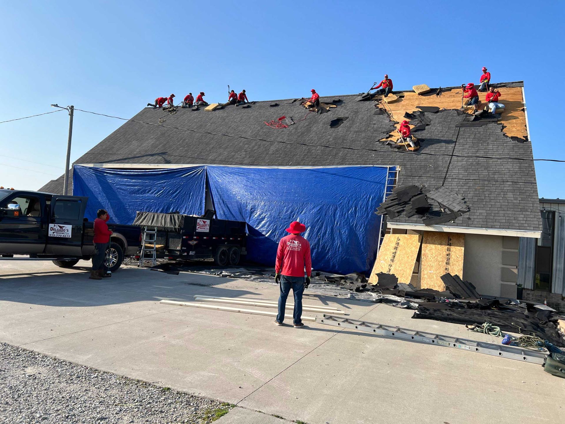 Workers repairing a roof with blue tarp covering part of a damaged building