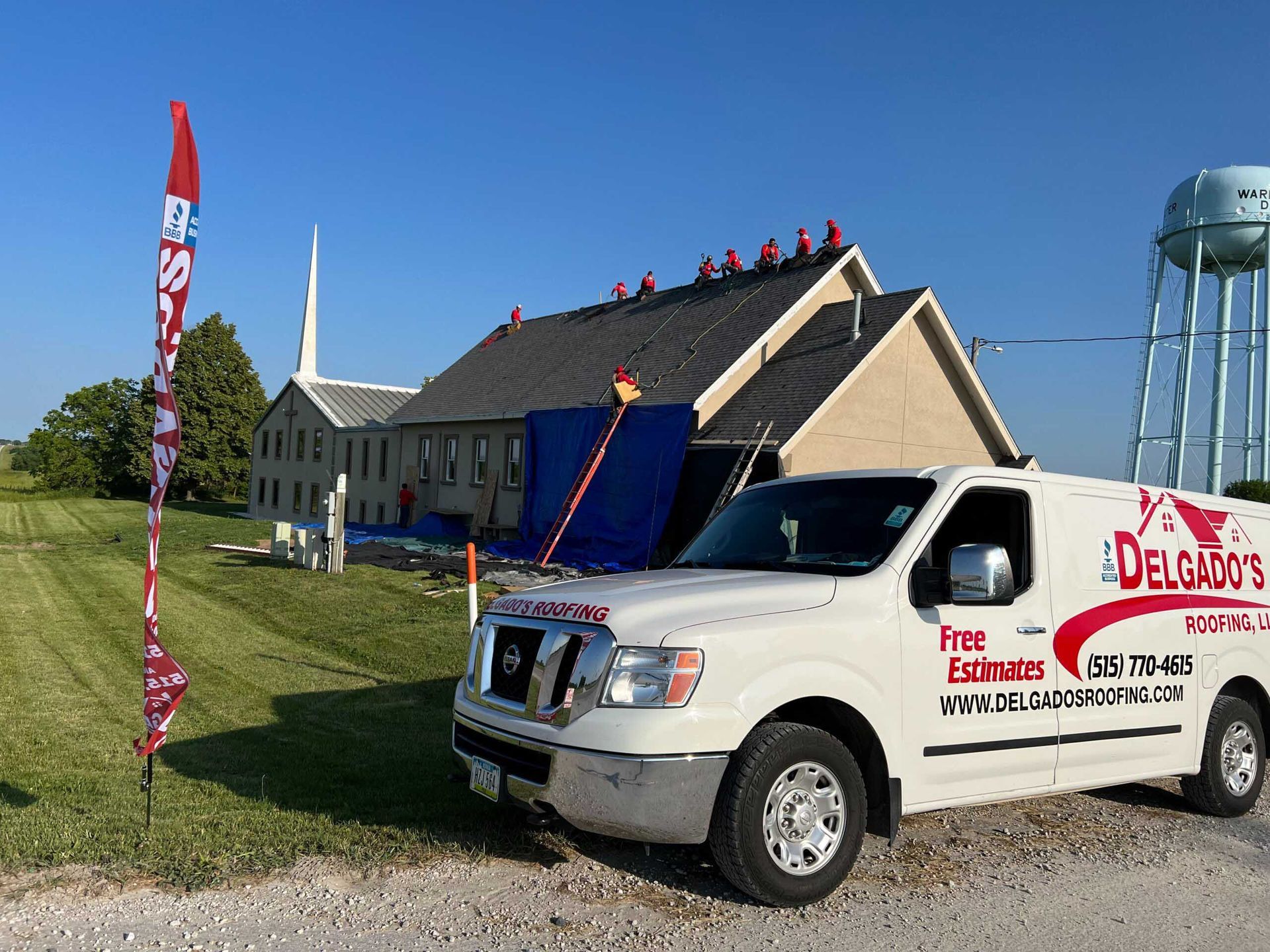 White delivery truck beside a church with a blue roof and red banners on a sunny grassy lawn