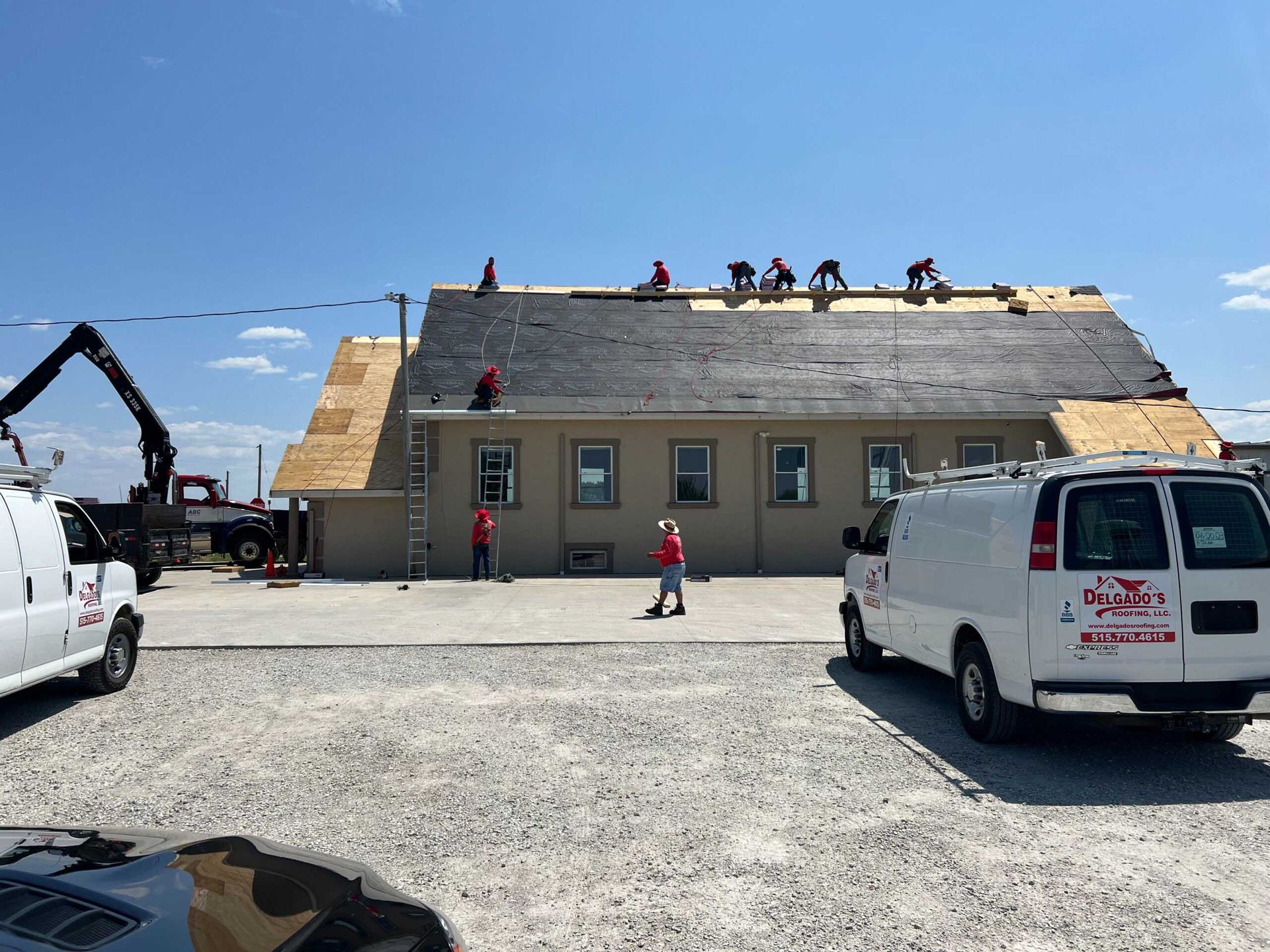 Roofers working on a house roof with two white vans parked in front on a gravel lot.