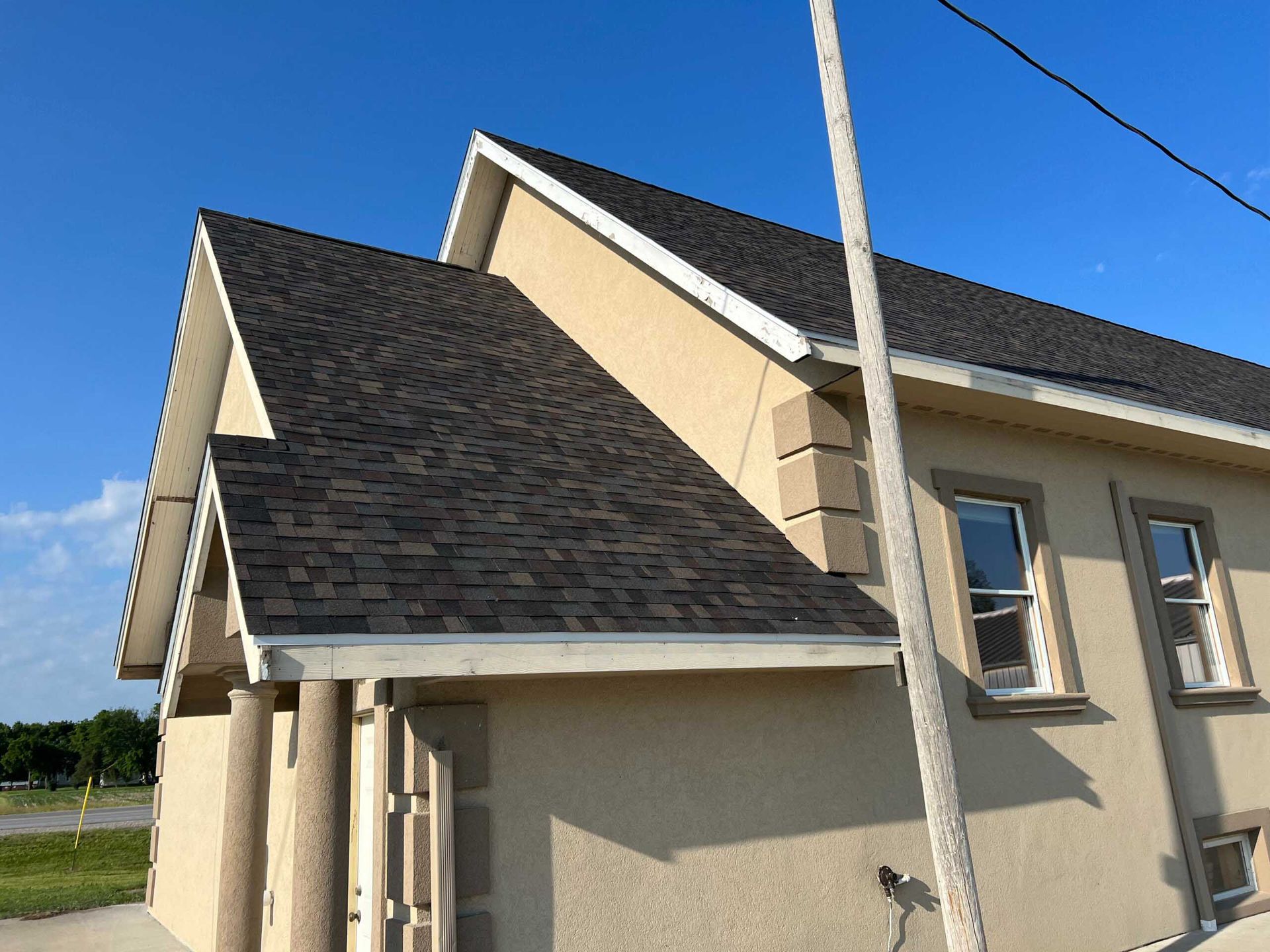 Beige house with steep dark shingle roof against a blue sky