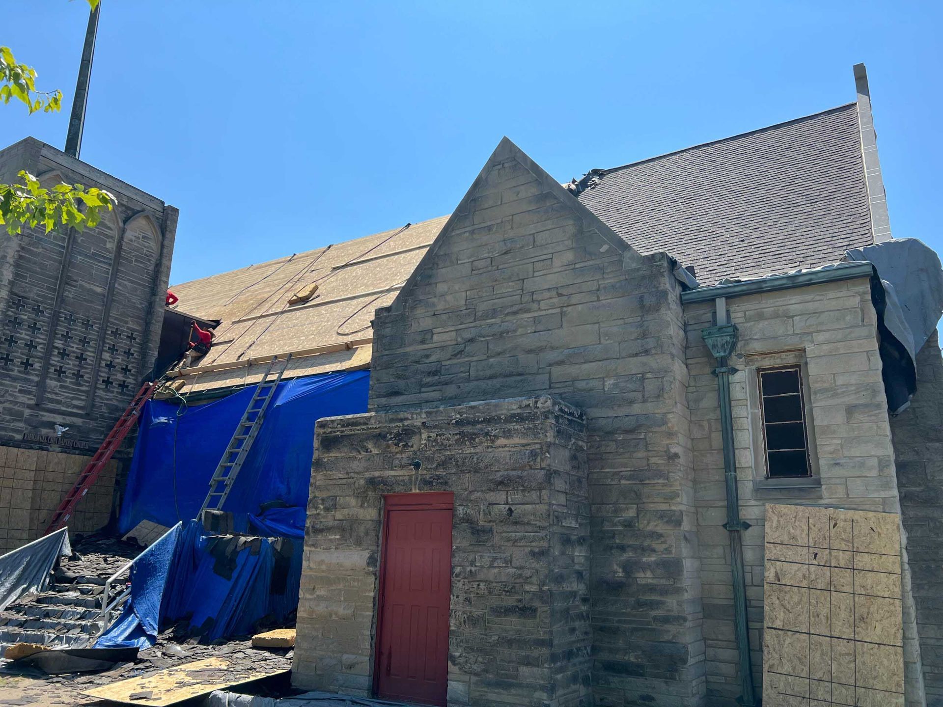 Old stone building with a red door beside a blue tarp-covered structure under a bright sky