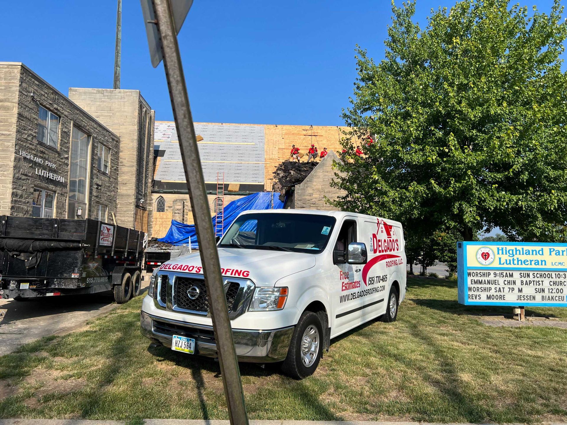 White utility truck parked on grass near a building and sign, with a tree and blue sky in the background