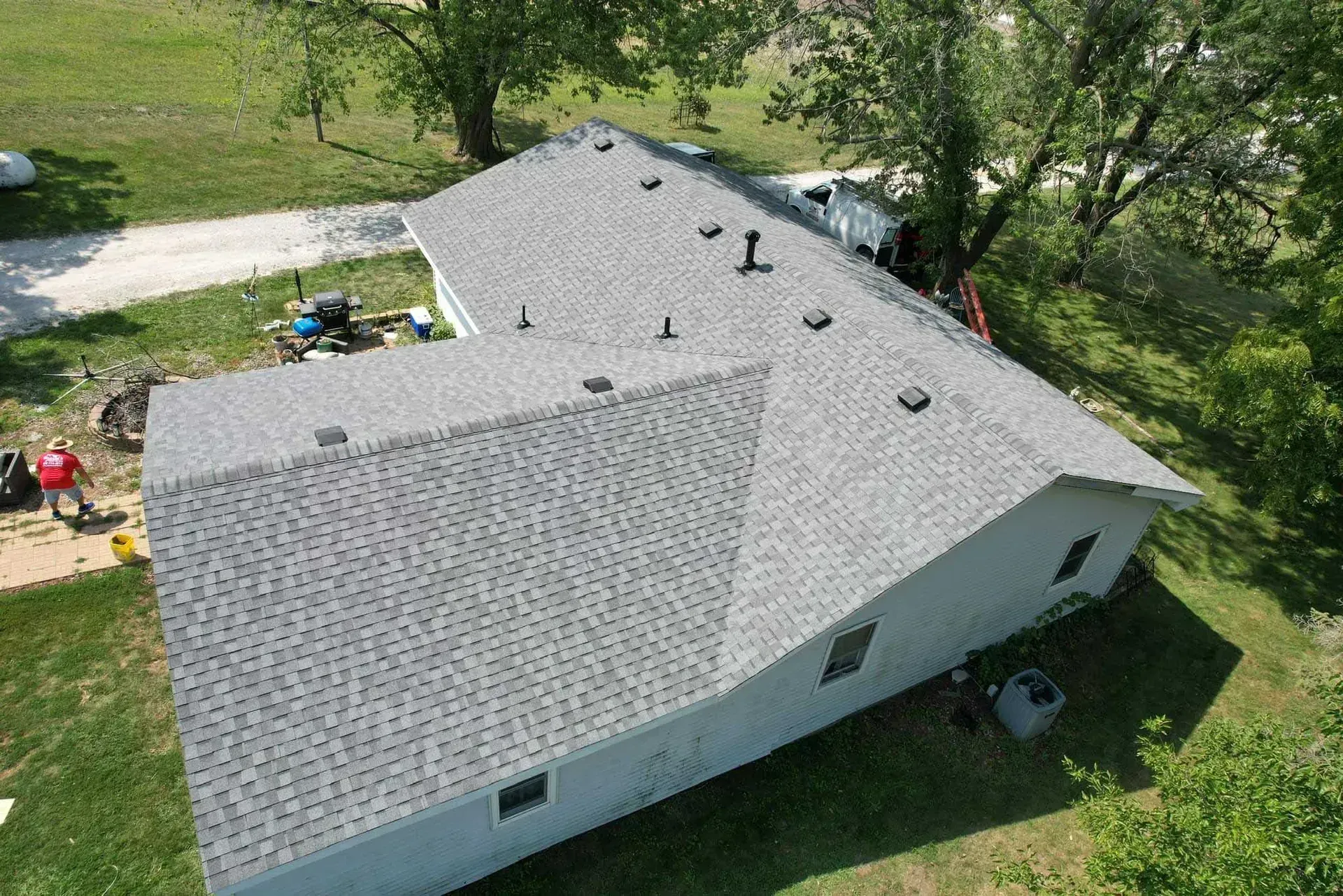Aerial view of a white house with a gray shingled roof surrounded by trees and lawn.