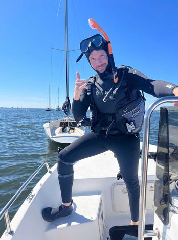 Man in a wet suit is standing on a boat in the water