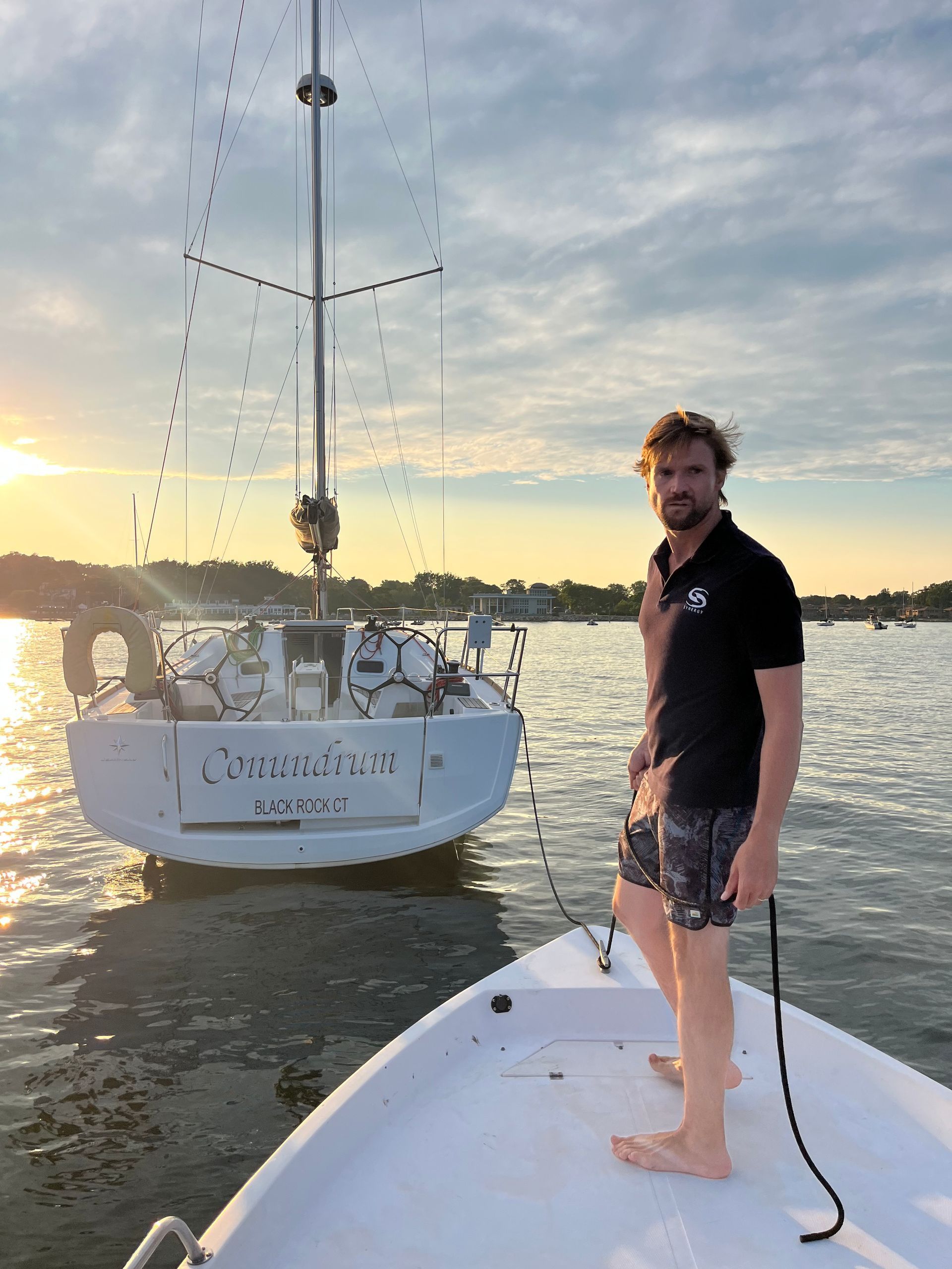 A man is standing on a boat in front of a sailboat