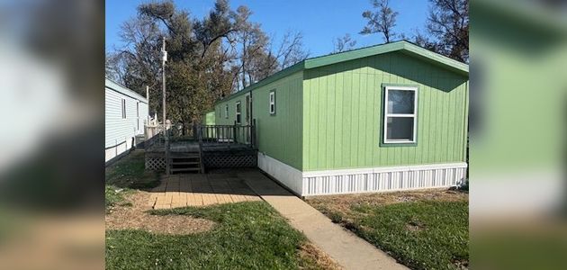 Green mobile home on a sunny day with a walkway in the foreground.