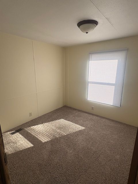 Empty bedroom with beige walls, brown carpet, and a window with blinds.