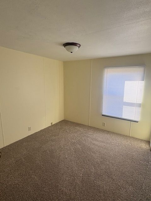 Empty room with beige walls, brown carpet, and a window with closed blinds.
