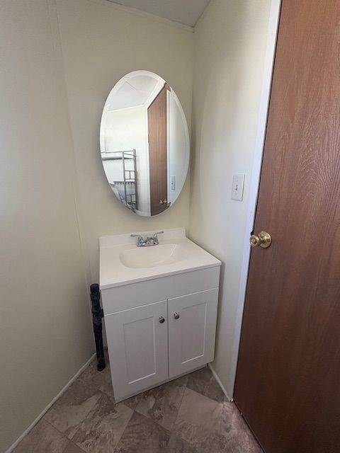 Small bathroom with a white vanity and oval mirror. A brown door is on the right.