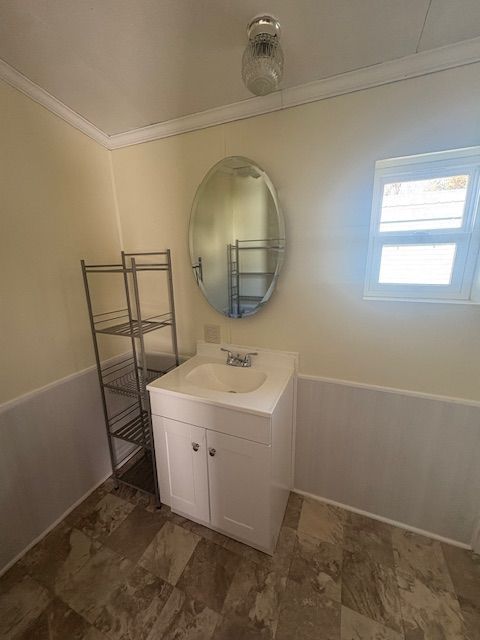 Bathroom with white vanity, oval mirror, small window, and wire shelving unit.