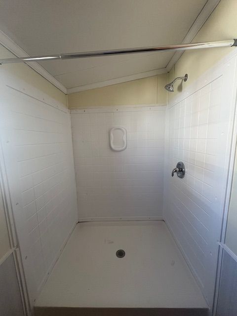 White-tiled shower with a showerhead, faucet, soap dish, and drain in the center of the base.