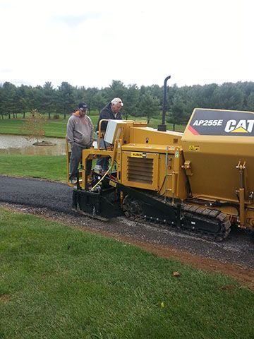 Two men are standing next to a cat asphalt paver.