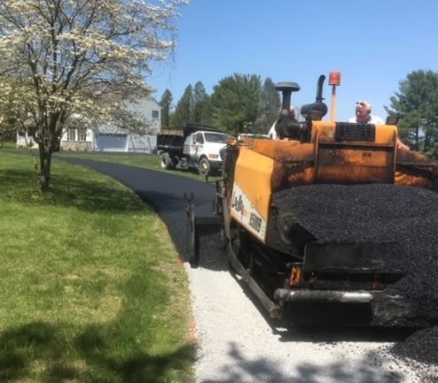 A man is driving a yellow and black asphalt paving machine