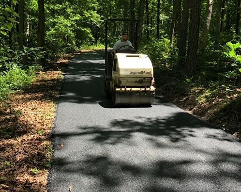 A man is driving a roller down a road in the woods.