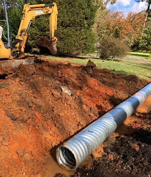 A large pipe is sitting in the dirt next to a yellow excavator.